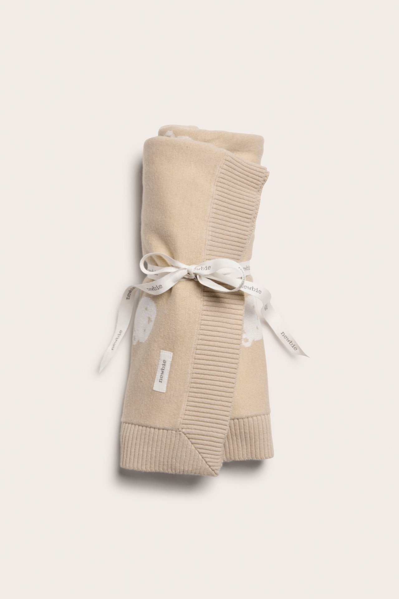 Front view of a rolled beige jacquard-knitted cotton blanket with a teddy bear pattern, tied with a white ribbon.