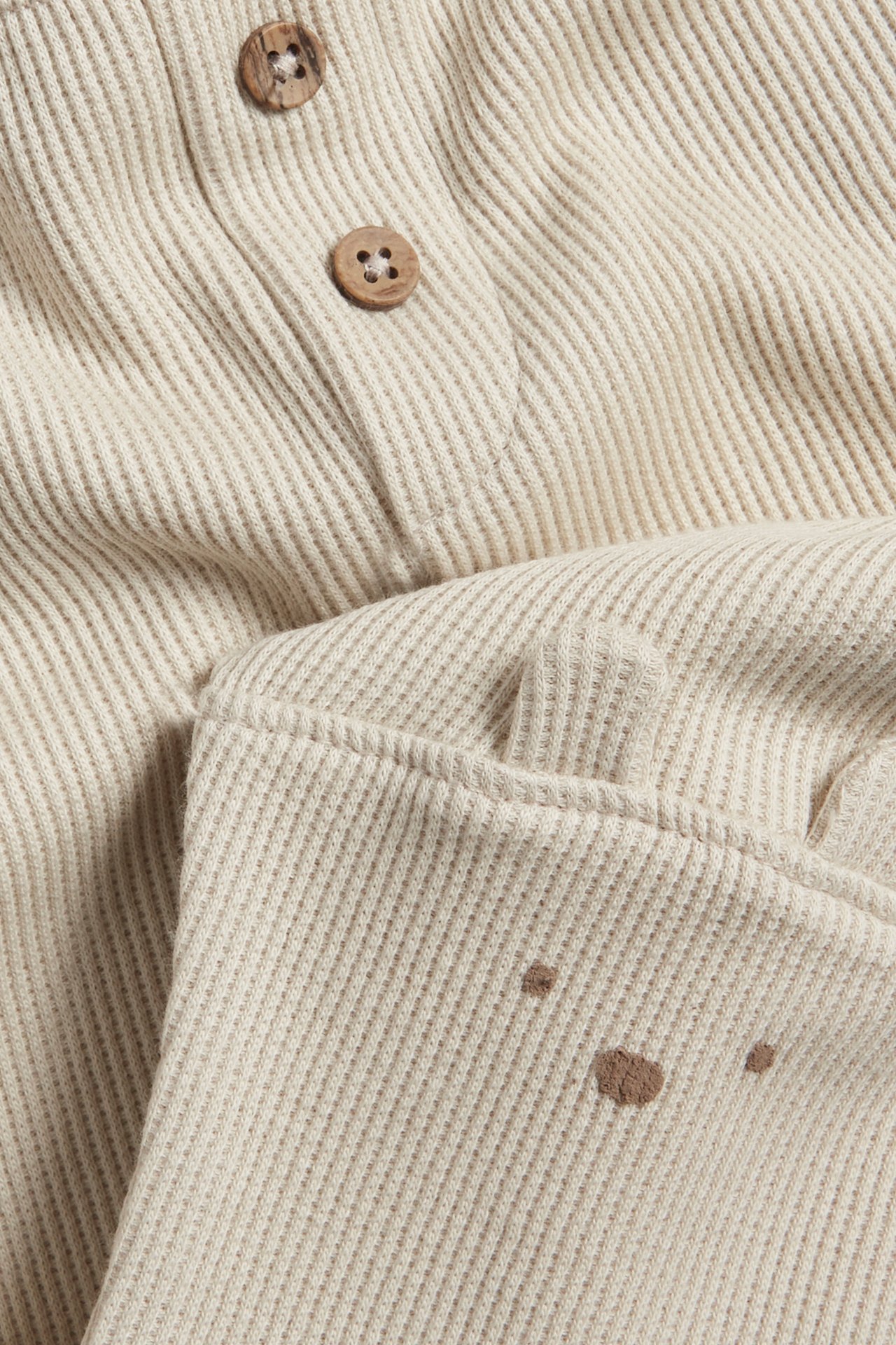 Nahaufnahme beiger Waffelstrick-Baby-Leggings mit dekorativen Holzknöpfen und einem Bären-Puffdruckgesicht mit Ohren.