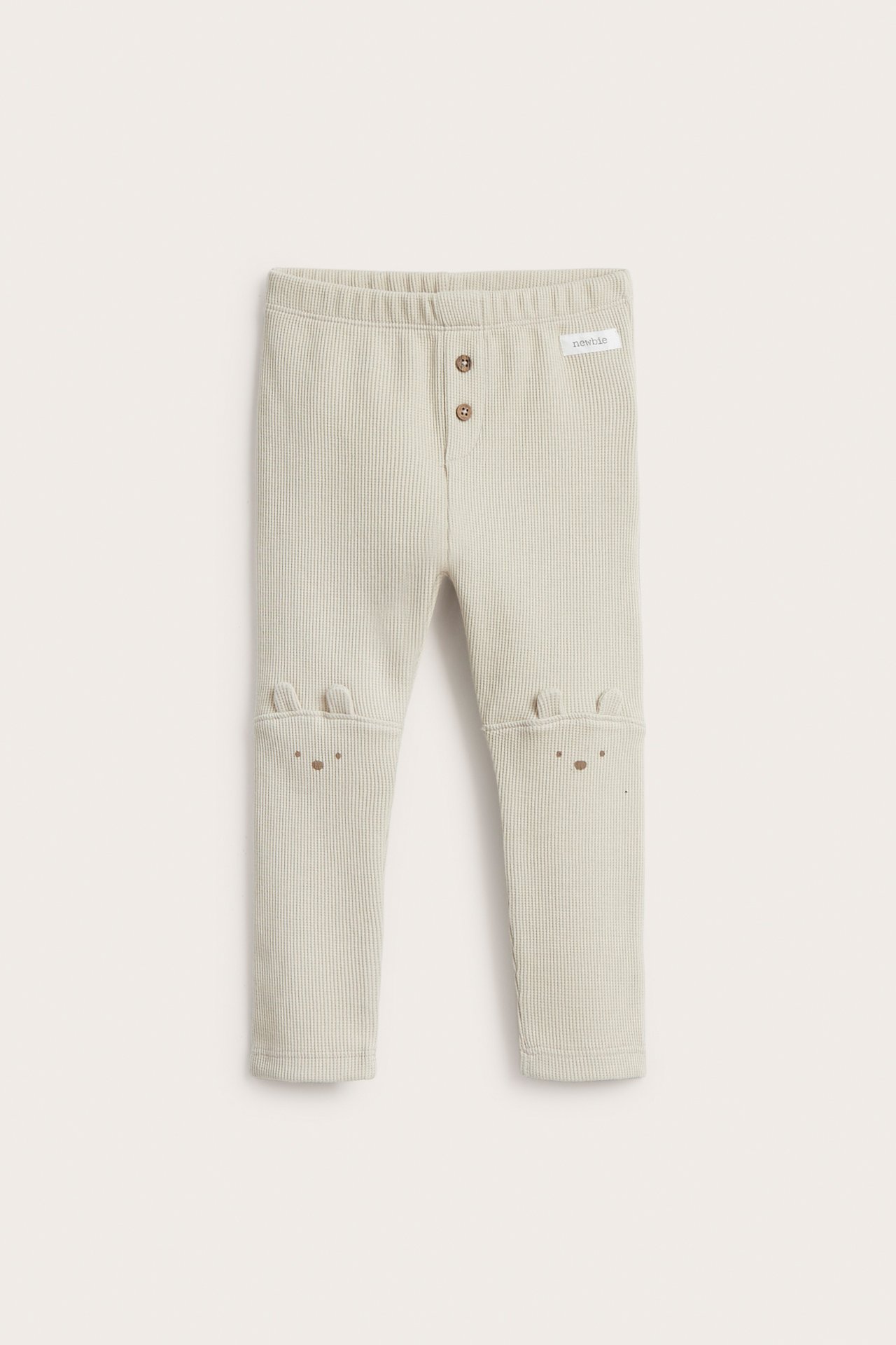 Vorderansicht: Beige Waffelstrick-Kinderleggings mit Zierknöpfen, Gummizugbund und aufgenähten Ohren an den Knien.