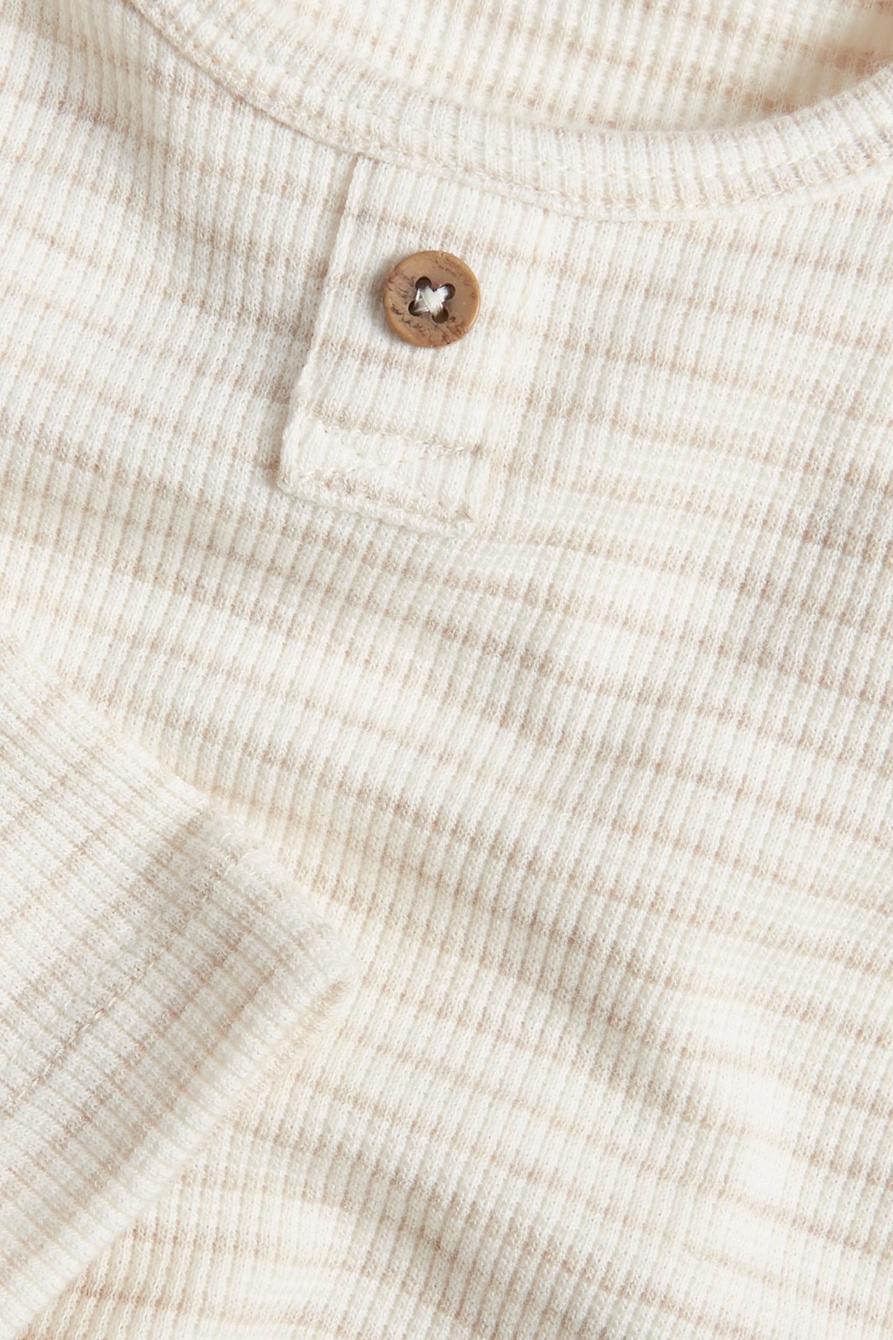 Close-up of a beige melange striped waffle baby bodysuit with a decorative wooden button.