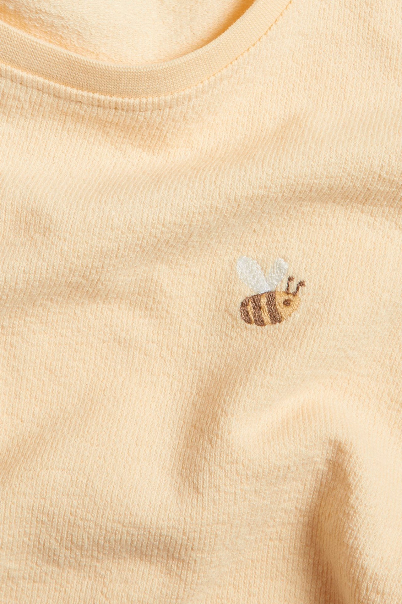 Nahaufnahme eines gelben Baumwoll-T-Shirts mit einer kleinen gestickten Biene vorne.