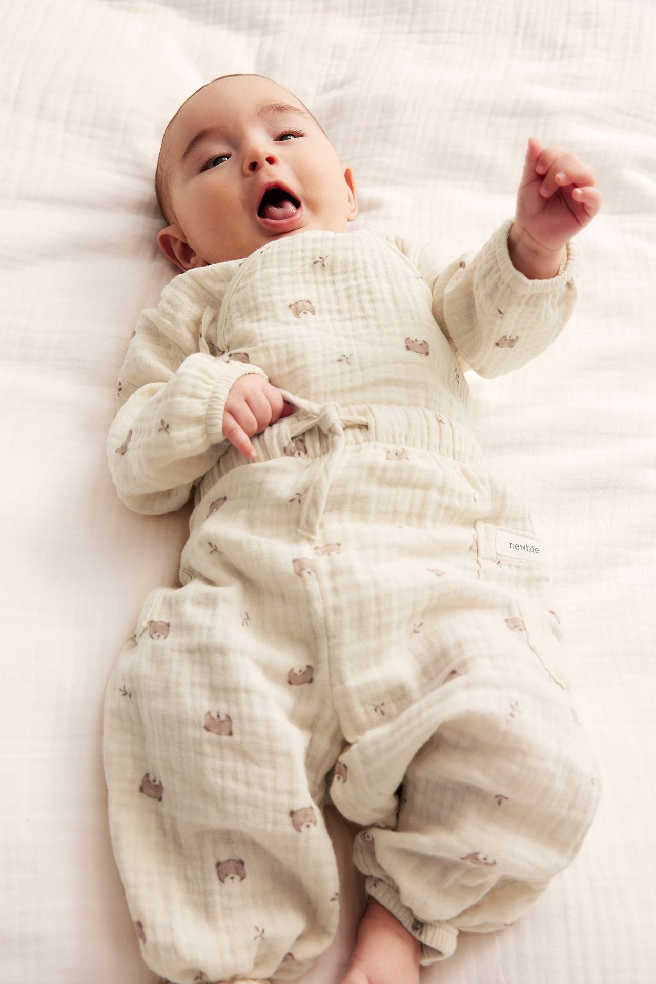 Front view: baby in light beige cotton muslin pants with bear pattern and matching long-sleeved top.