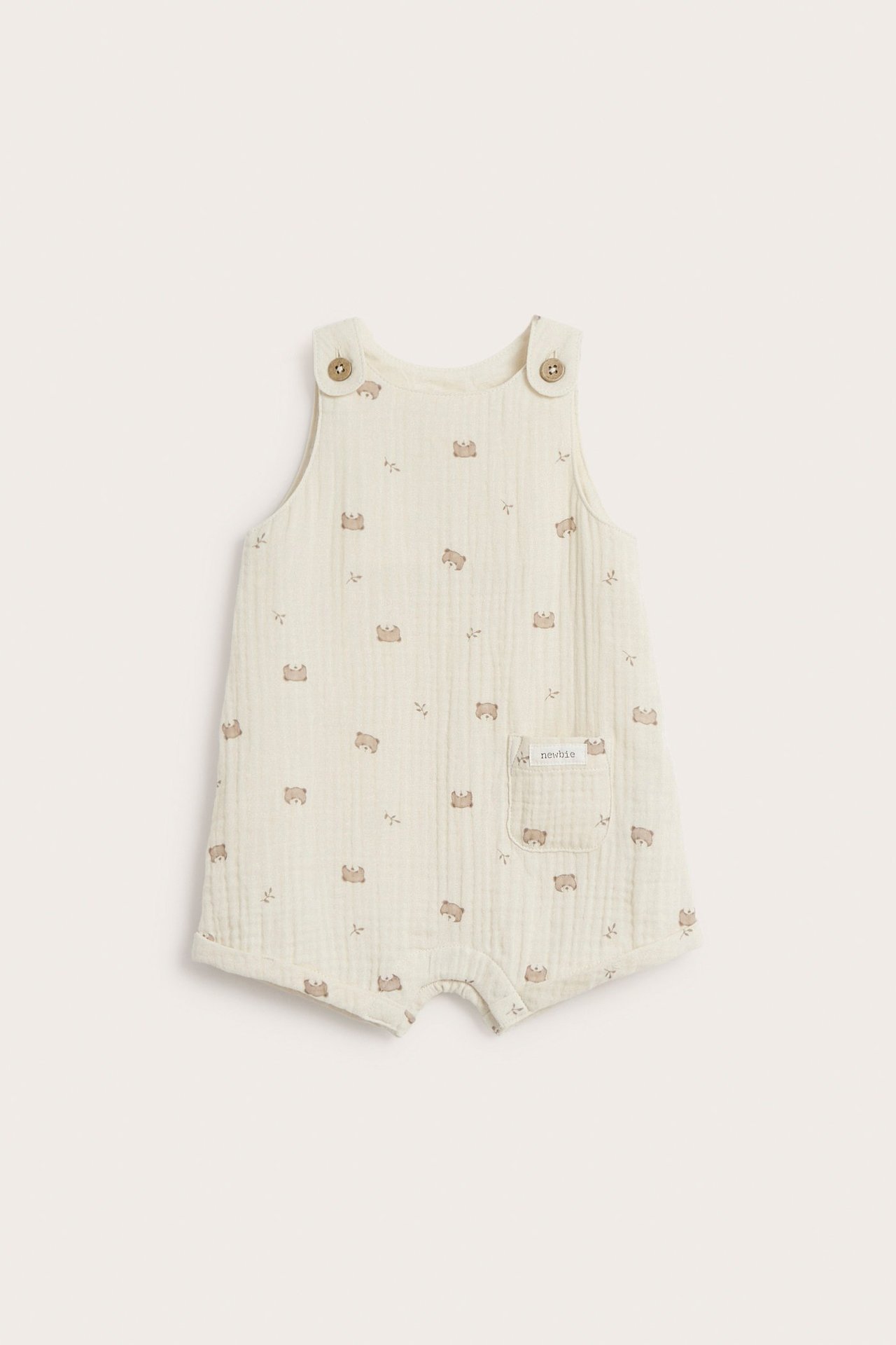 Front view: Light beige baby cotton playsuit with a teddy bear pattern, pocket, and shoulder buttons.
