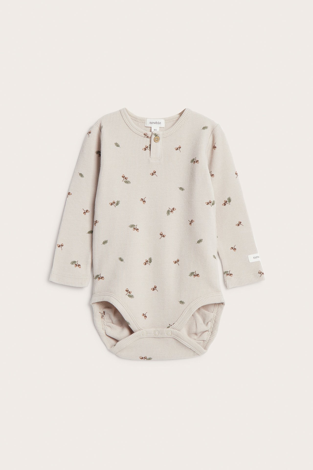 Front view of a beige waffle knit baby bodysuit with long sleeves, acorn pattern, and front buttons.