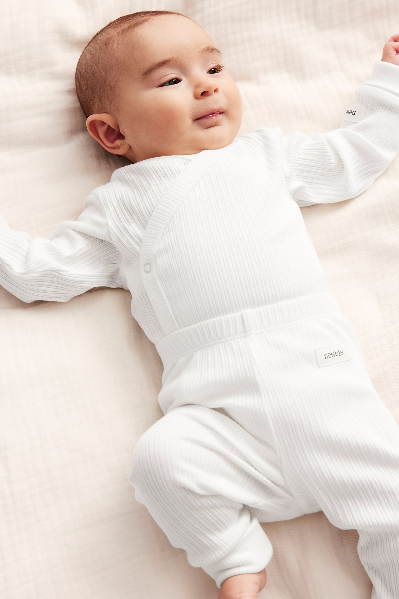 Top-down view of a baby wearing an off-white ribbed wrap-over bodysuit with snap buttons and matching ribbed pants.