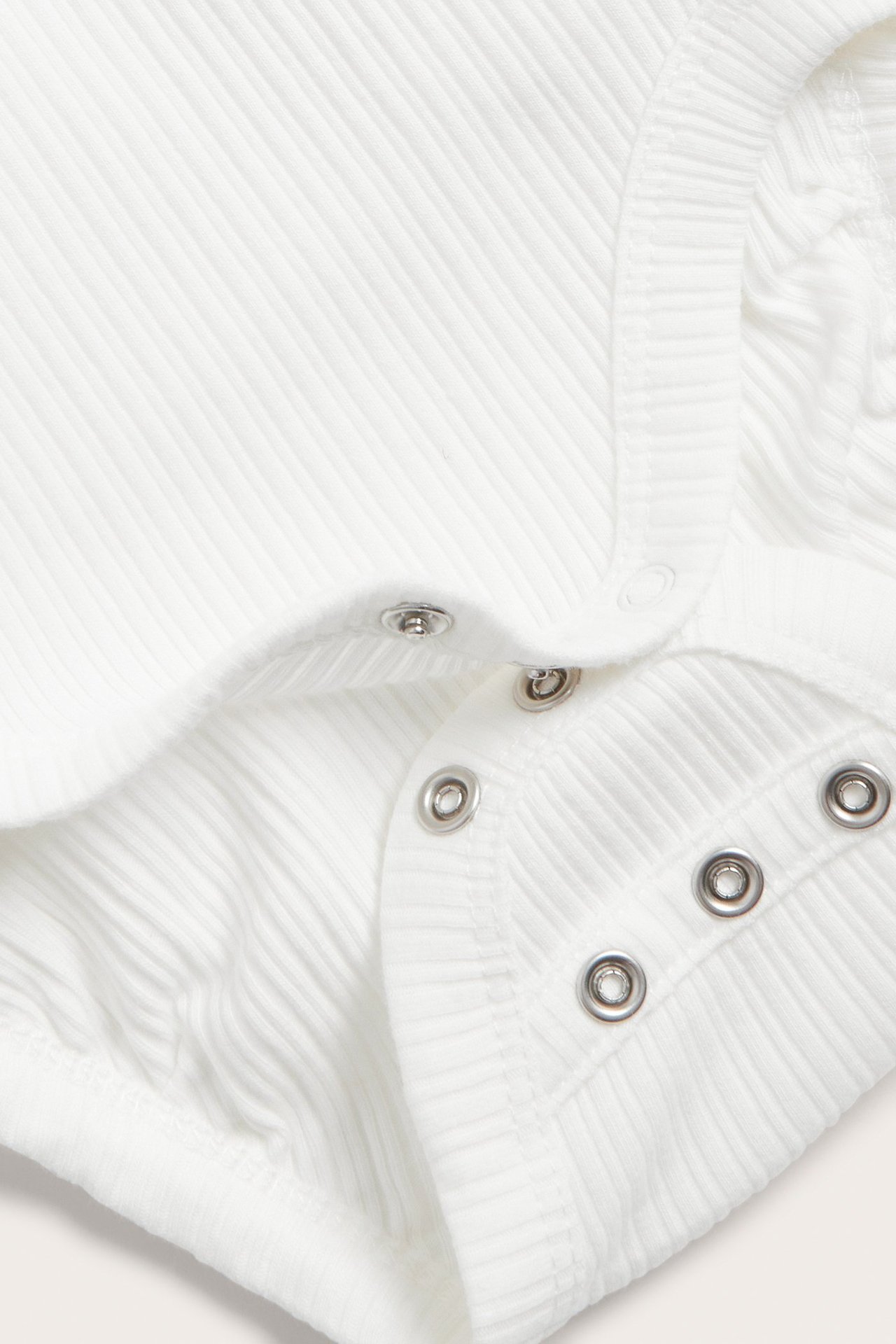 Close-up of an off-white ribbed wrap-around baby bodysuit with silver snap buttons at the crotch.