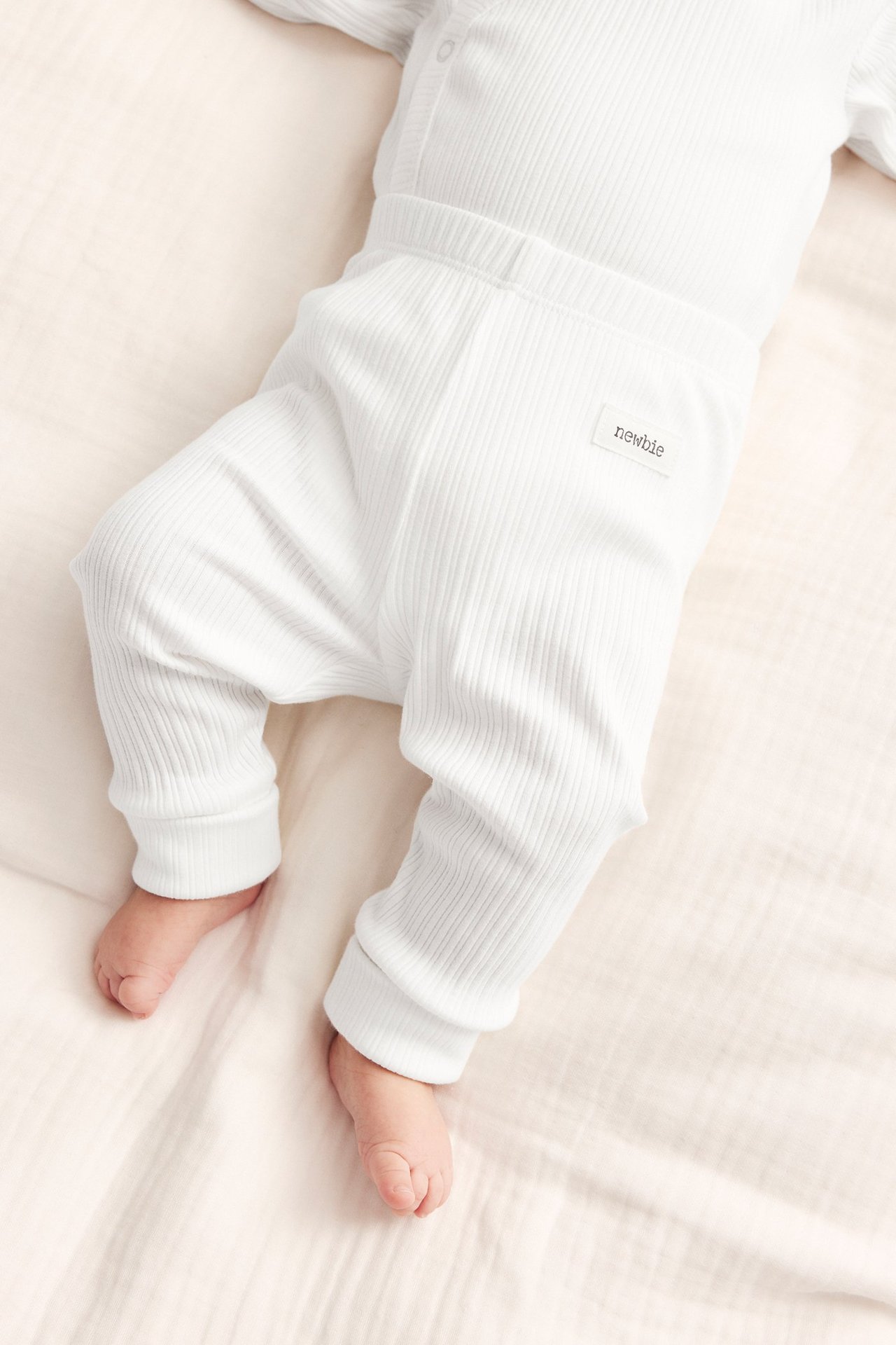 Top view of a baby wearing off-white ribbed leggings with folded cuffs and a matching ribbed top.