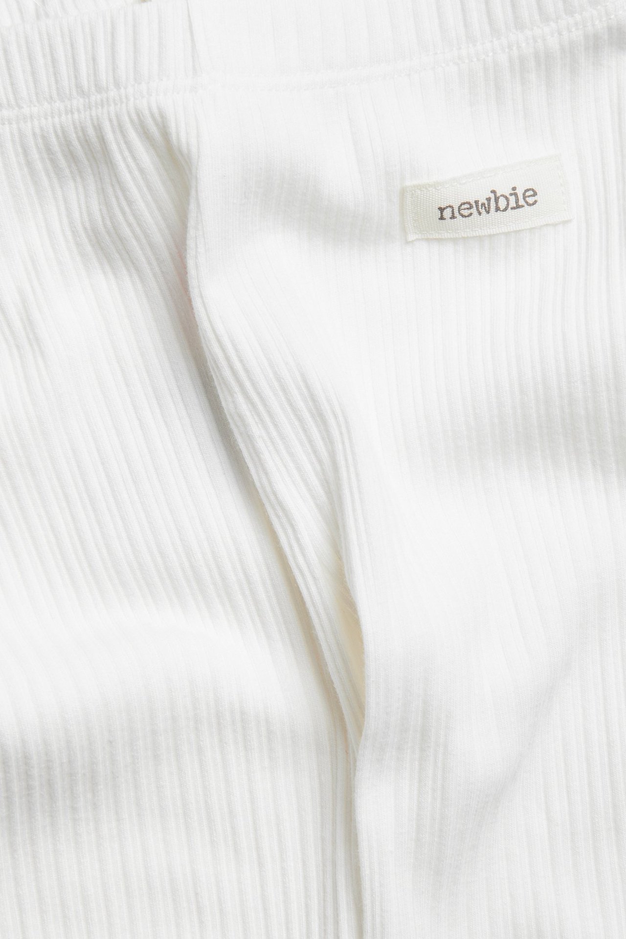 Close-up of offwhite ribbed baby leggings with a "newbie" tag.