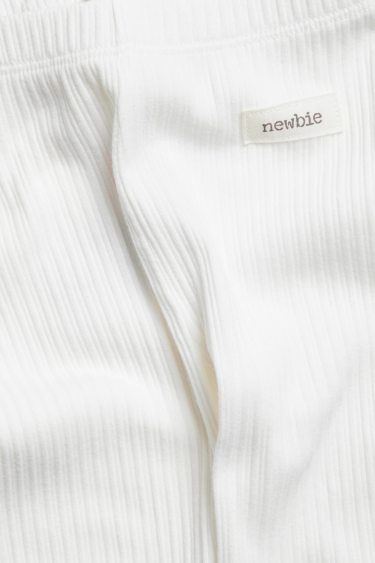 Nahaufnahme von cremeweißen gerippten Neugeborenen-Leggings mit elastischem Bund und einem Newbie-Etikett.