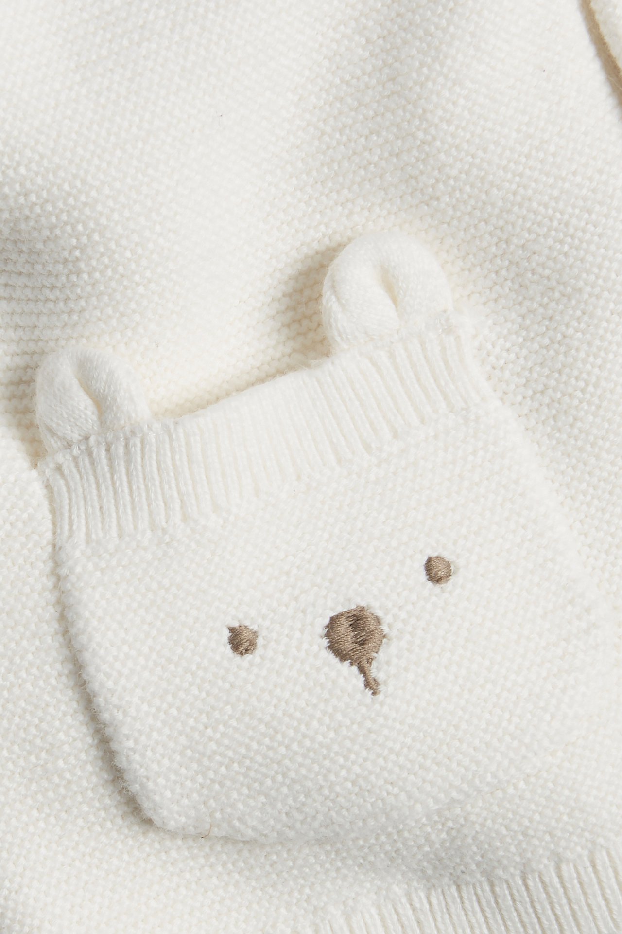 Close-up of off-white knitted baby cardigan, featuring pocket with embroidered bear face and ears.