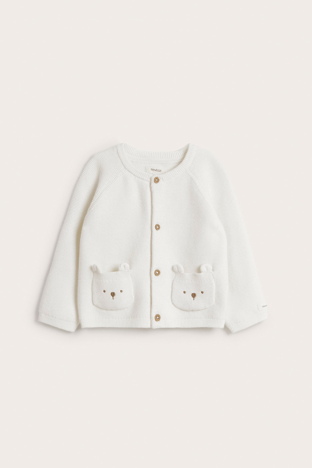 Front view of an offwhite knitted baby cardigan with bear-eared pockets and brown buttons.