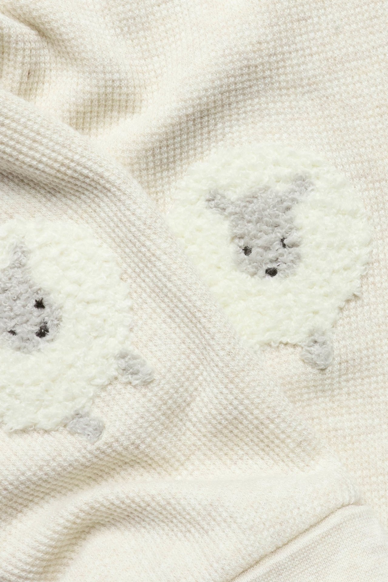 Close-up of beige melange waffle-knit leggings with fluffy white and grey sheep appliqués.