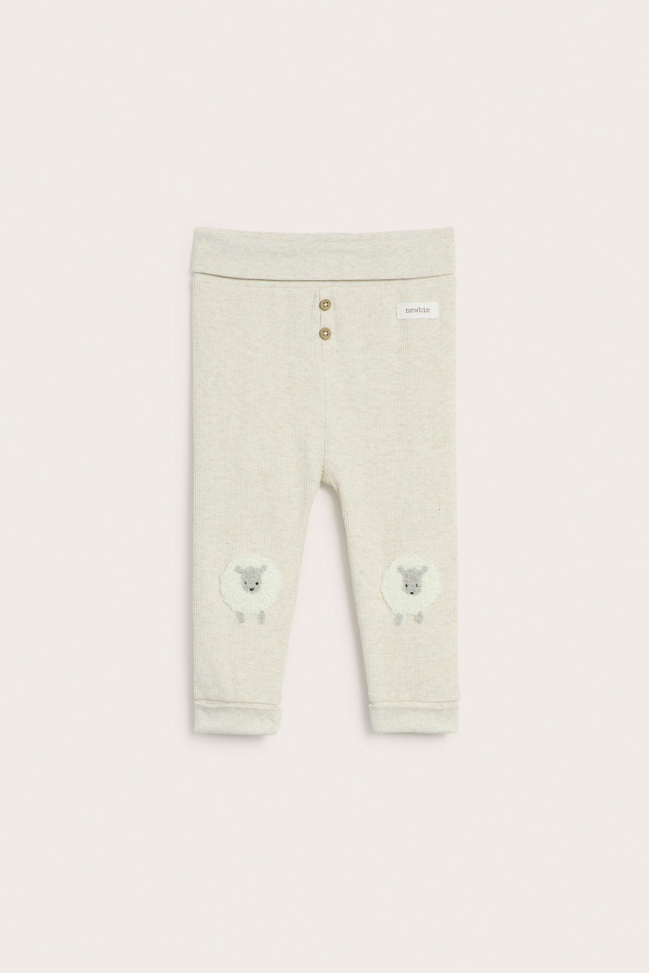 Front view of beige melange waffle-knit baby leggings with sheep knee patches and decorative buttons.