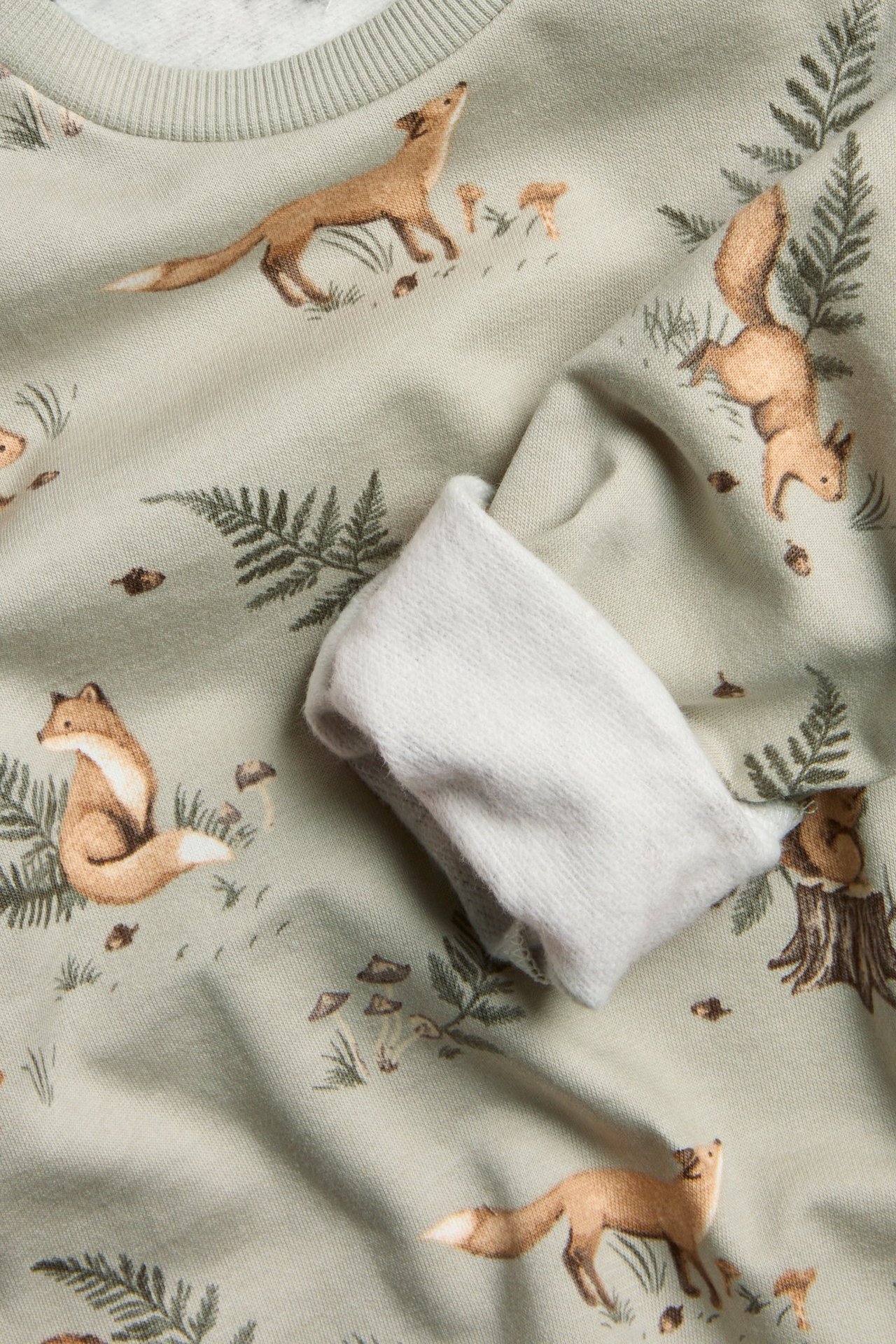 Nahaufnahme eines hellgrünen Kinder-Baumwollsweatshirts mit Waldtiermuster und Rippbündchen.