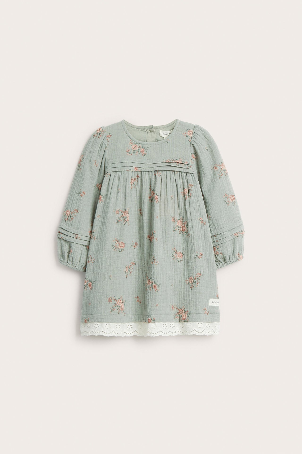 Front view: Kid's green woven cotton dress with pink floral print, pintucks, and white lace hem.