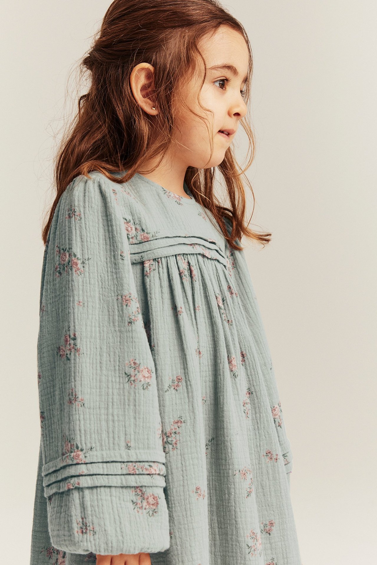 Side view of a kid wearing a light green cotton dress with small pink floral print and pintucks.