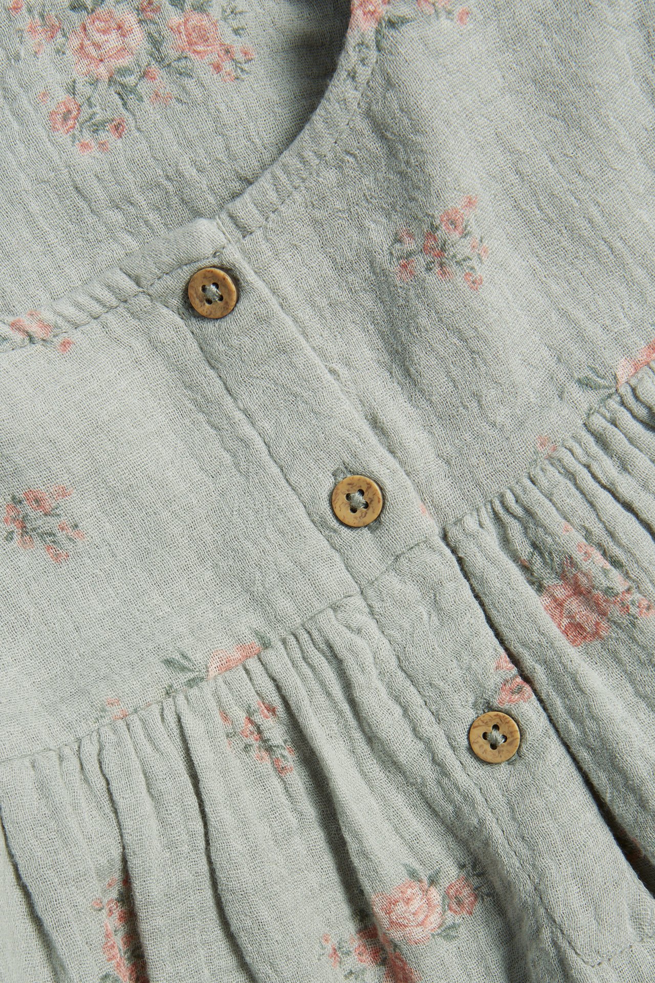 Nahaufnahme eines hellgrünen gewebten Baumwollkleides mit kleinen rosa Blumen und Holzknöpfen.