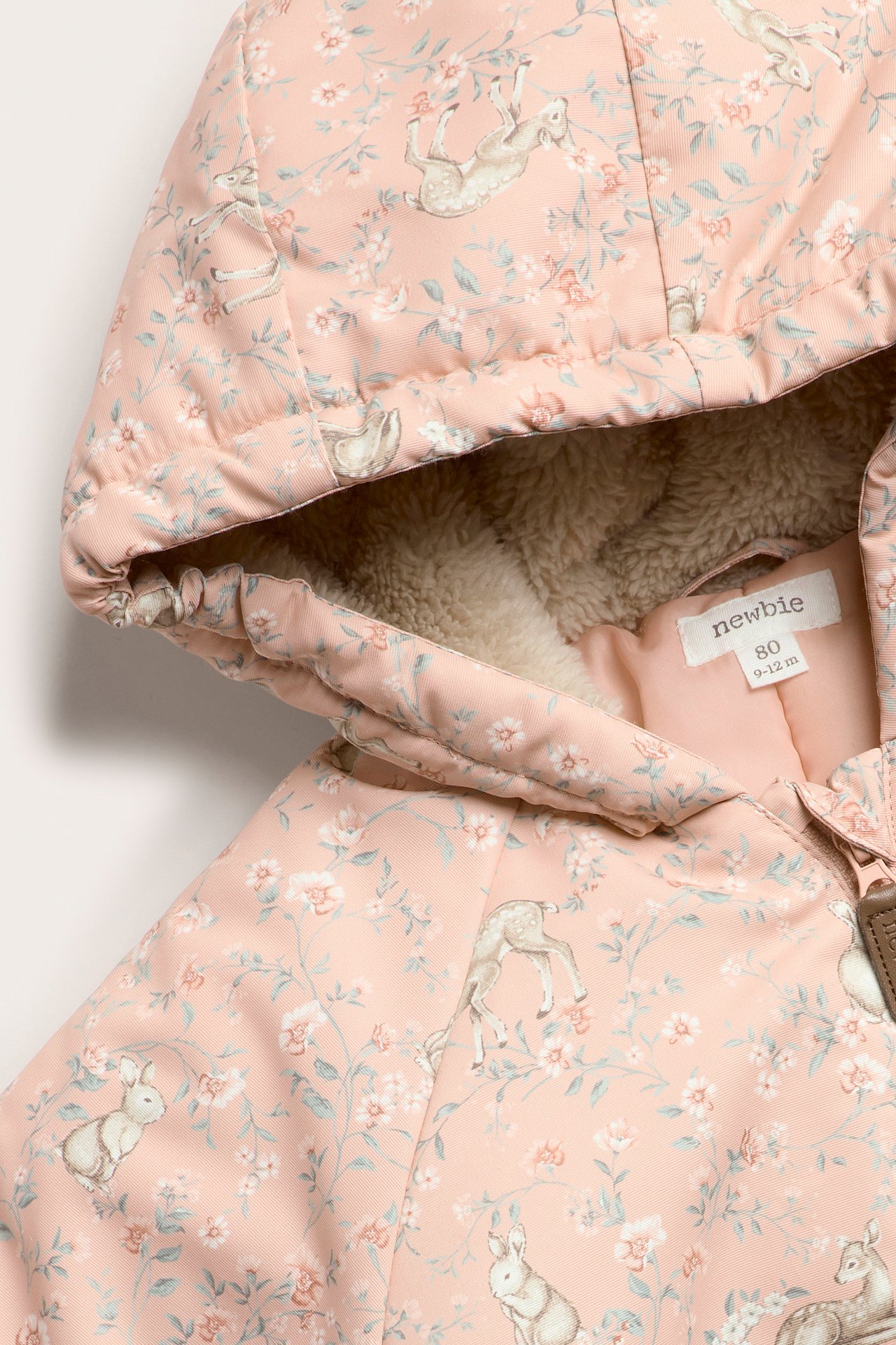 Close-up of a baby's pink windproof hooded coverall with floral, bunny, and fawn print, lined with beige fluffy material.
