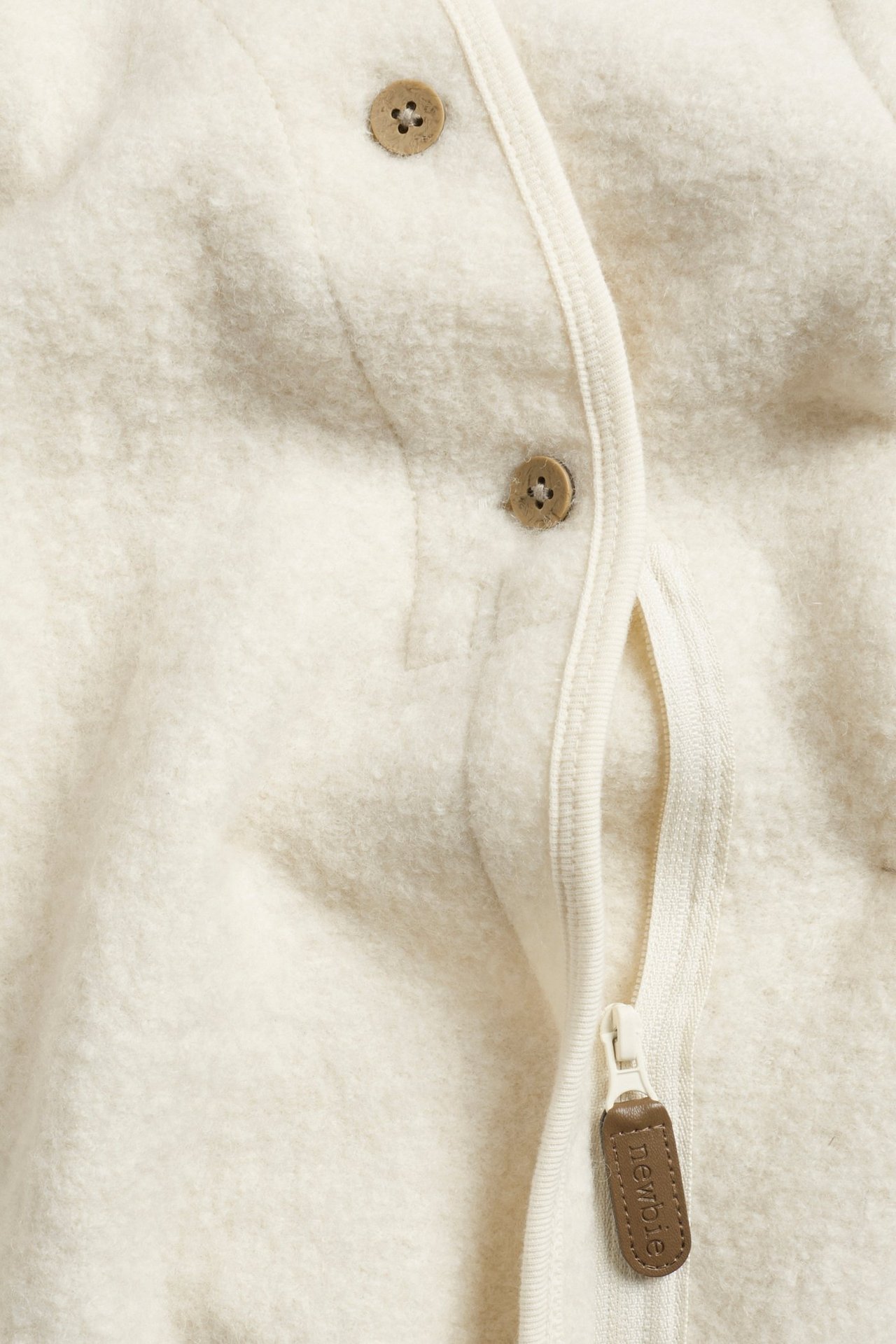 Close-up of a light beige wool baby overall with a zipper and two brown buttons.