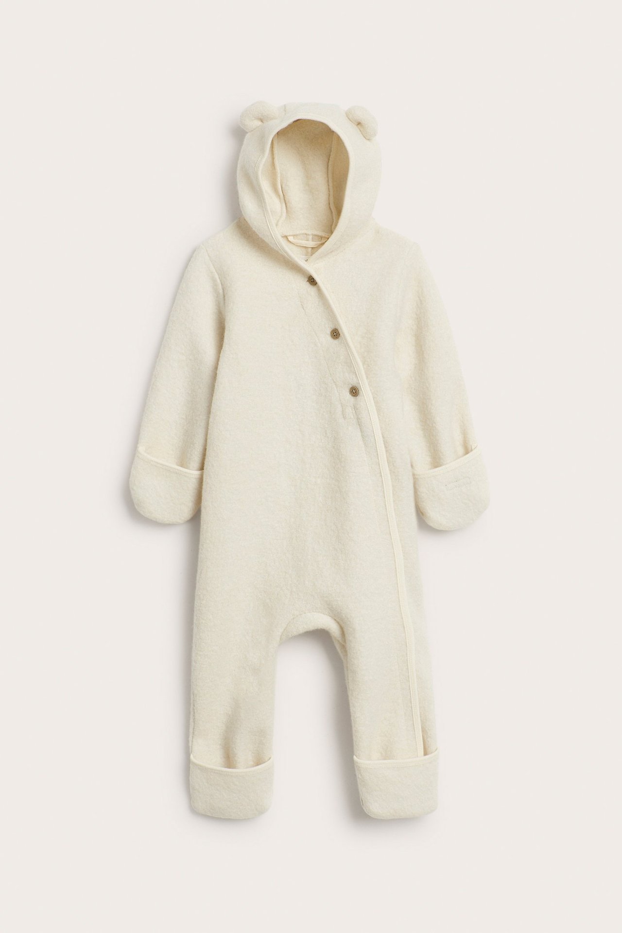Front view: Light beige wool baby overall with ear hood, front buttons, zipper, and fold-over cuffs.