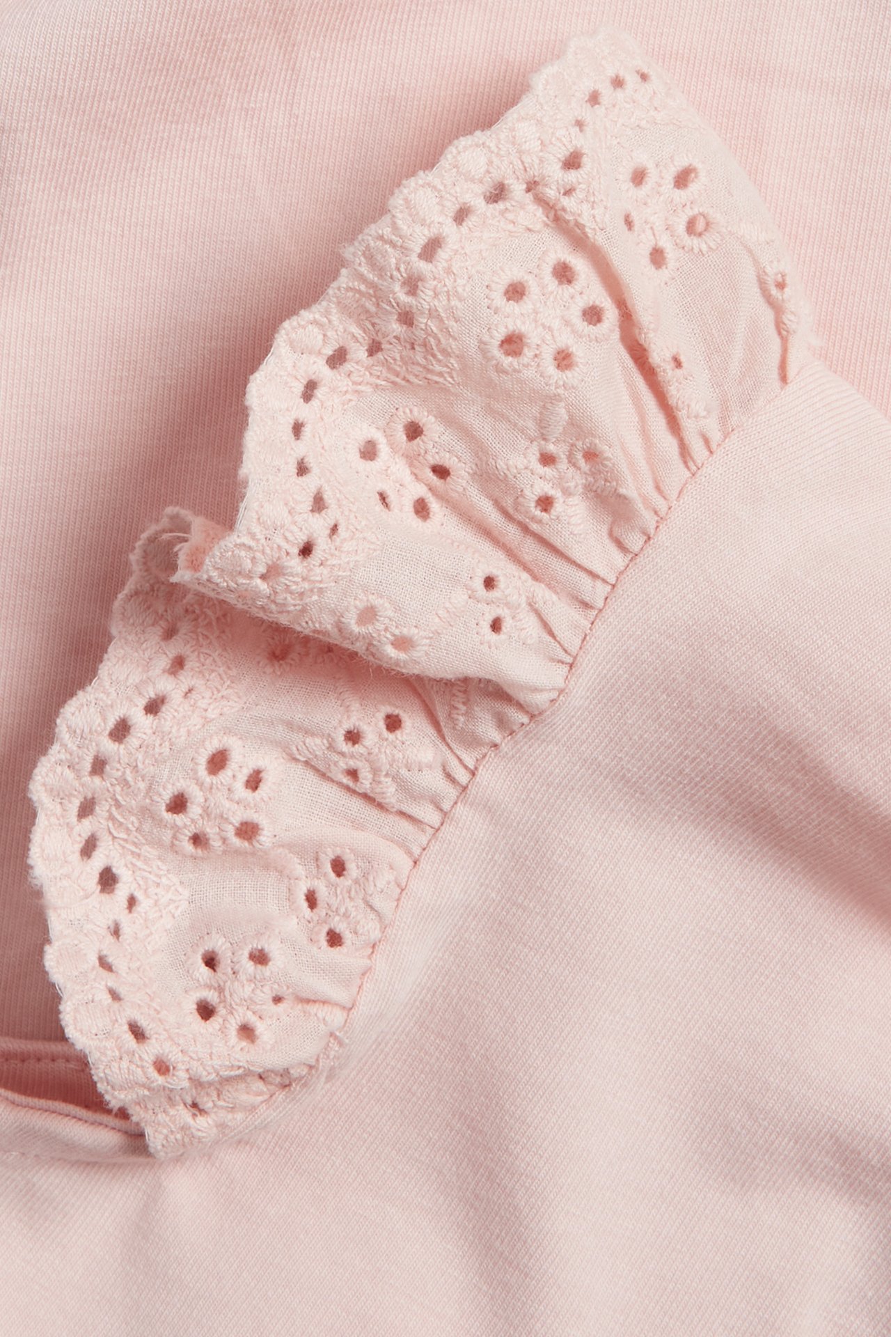 Close-up of a light pink baby body with a ruffled cotton lace sleeve.