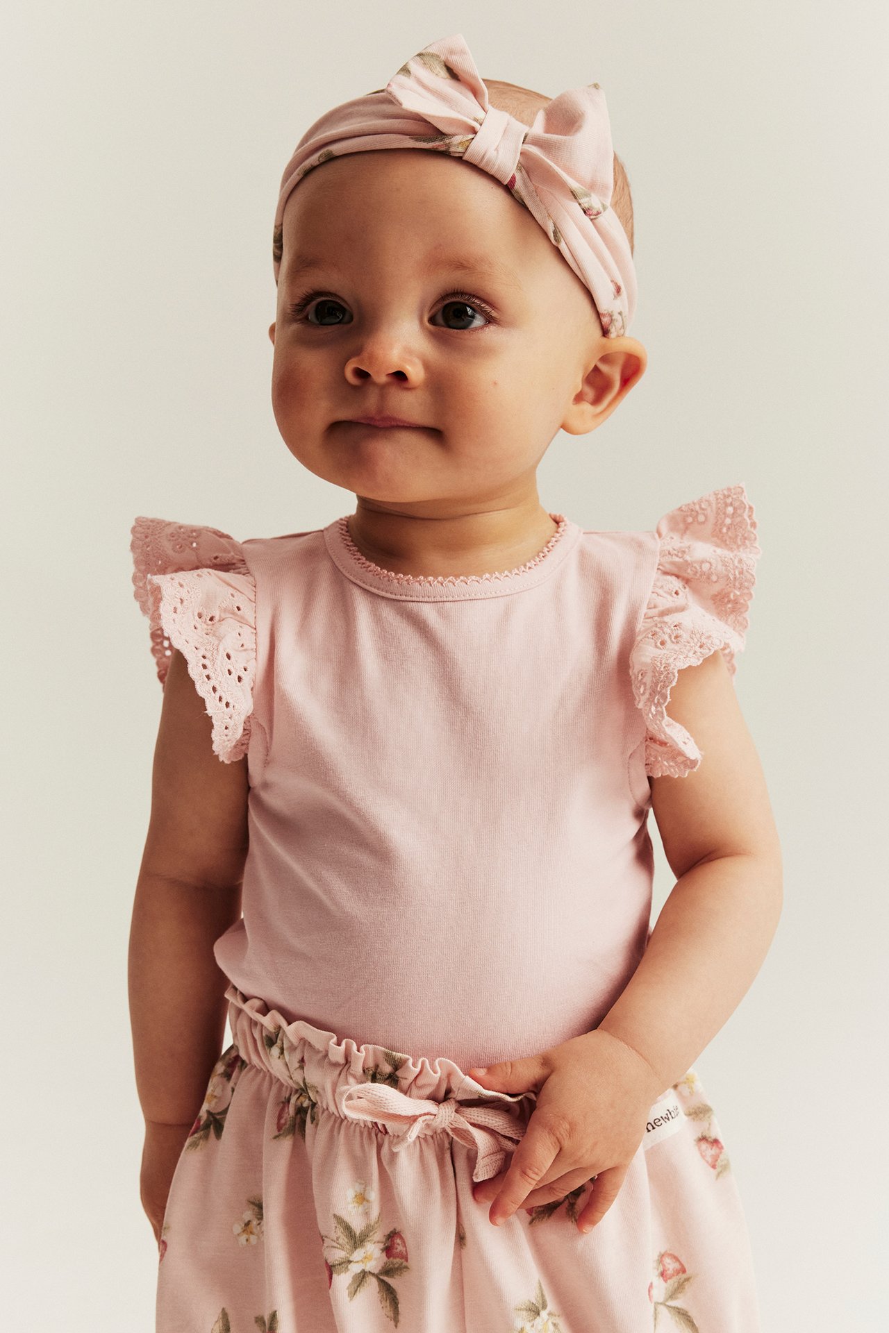 Light pink short-sleeved body with lace ruffle sleeves, matching patterned headband and shorts.