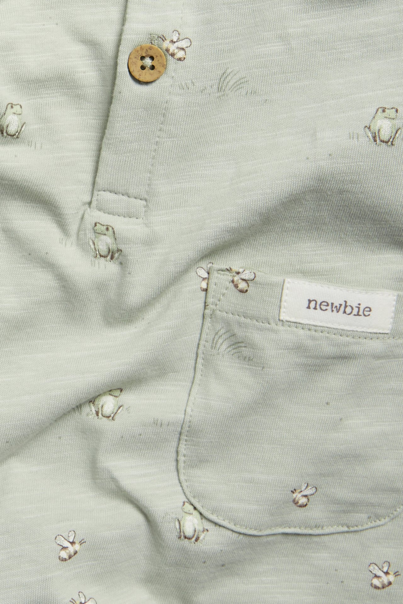 Close-up of a baby's green cotton slub jersey romper with frog and bee pattern, button, and pocket.