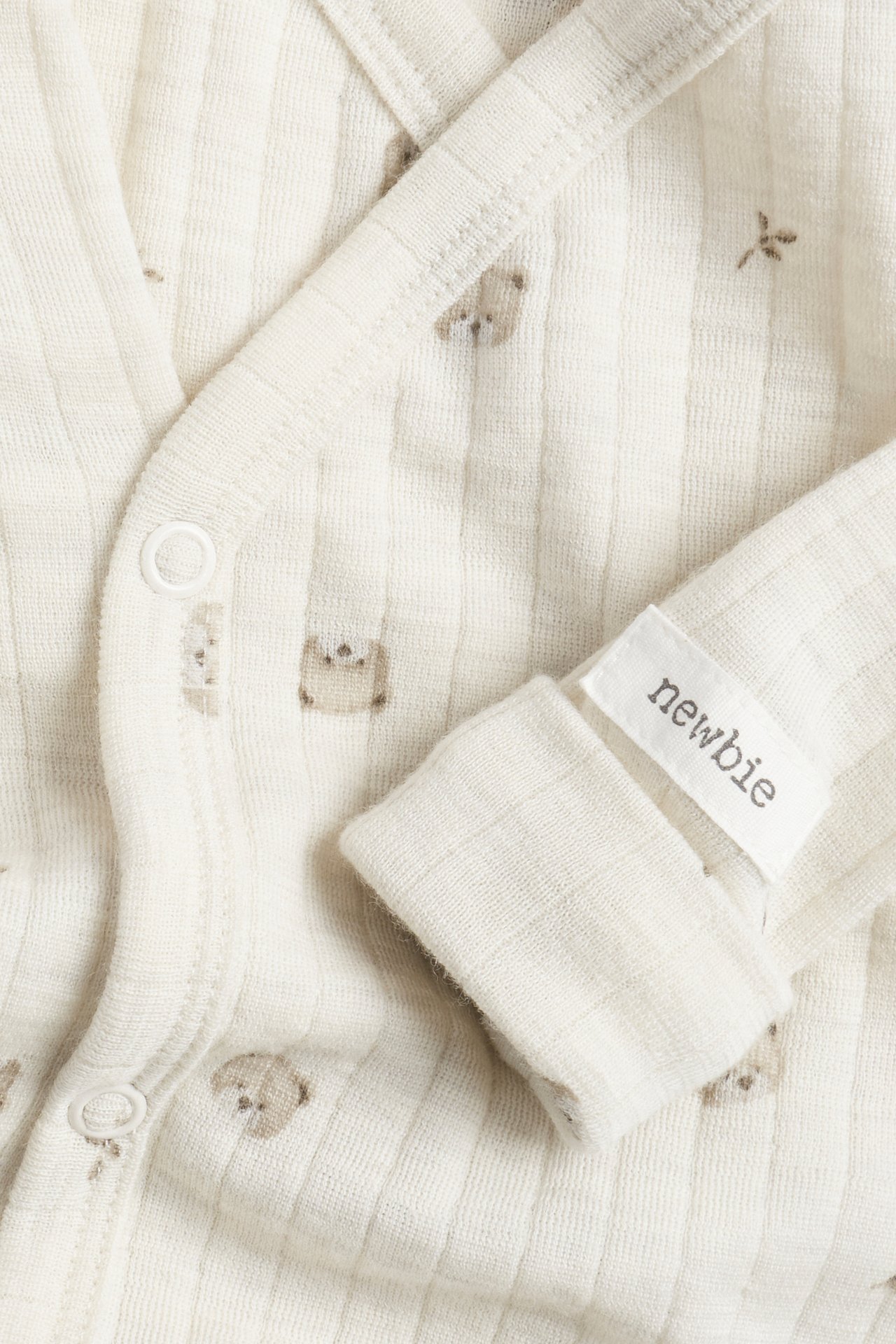 Nahaufnahme eines gerippten cremefarbenen Baby-Wickelbodys mit Bärchenprint und Druckknöpfen.