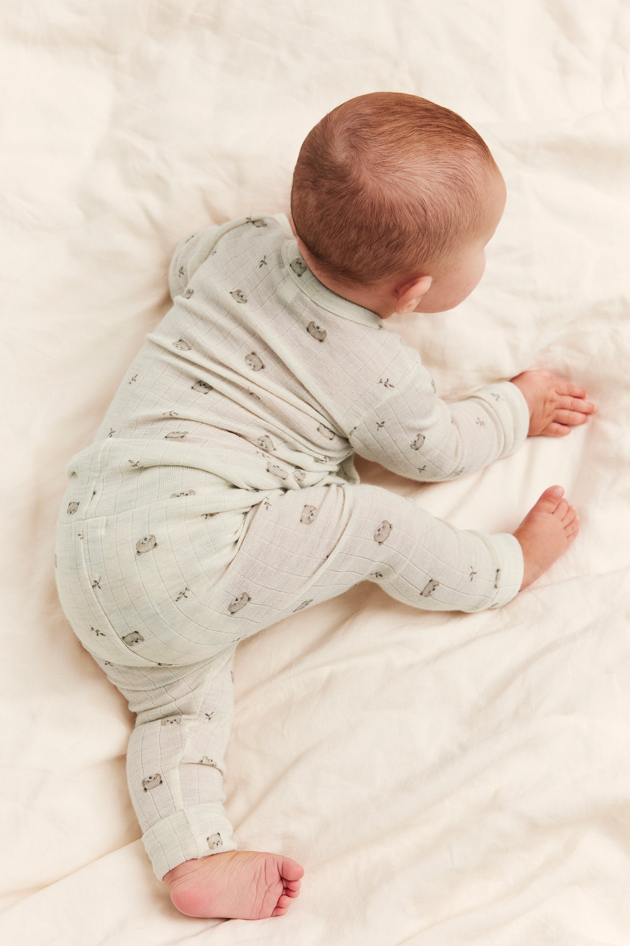 Overhead view of a baby in a light grey-green ribbed two-piece outfit with animal prints.