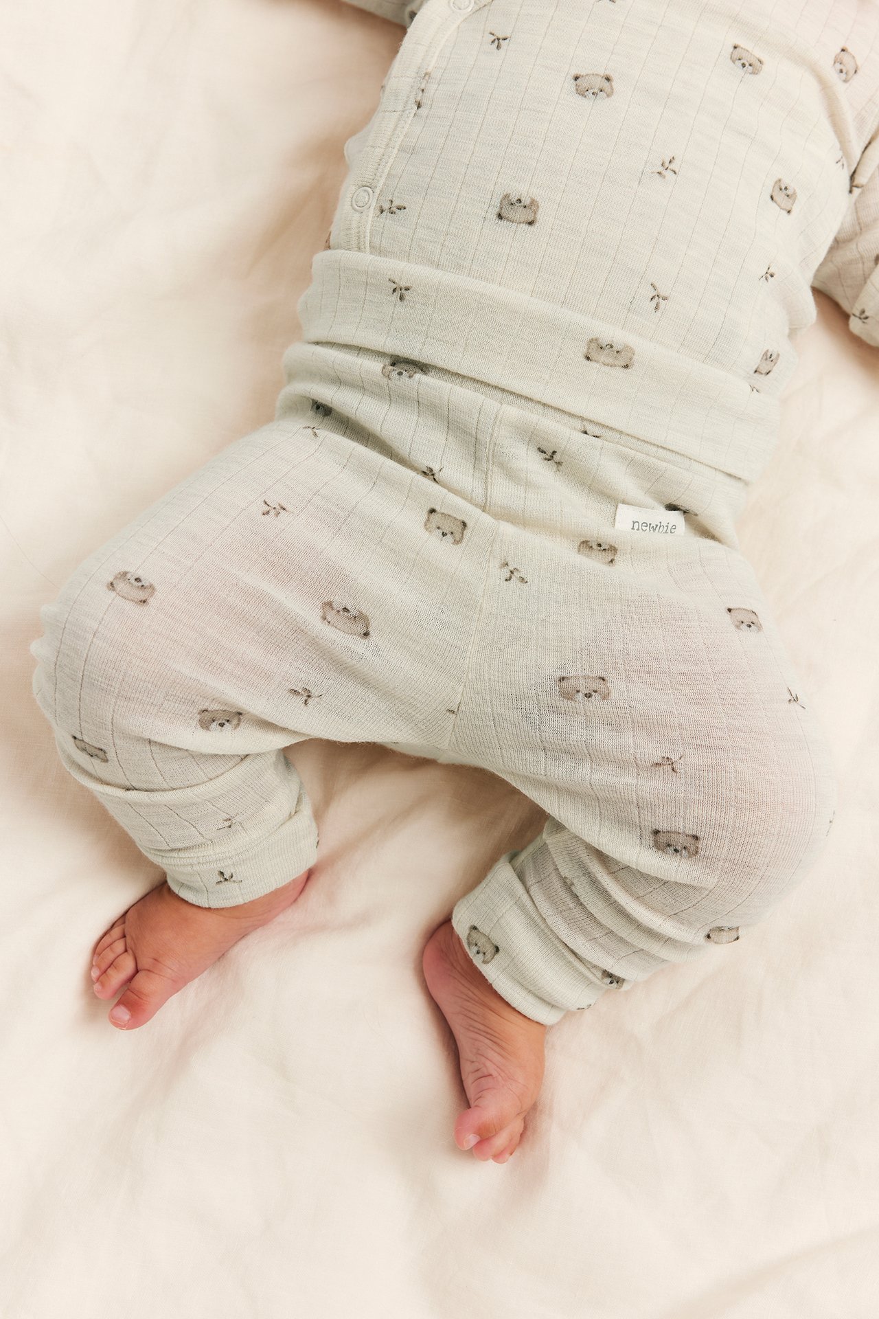 Nahaufnahme Baby in hellgrünem geripptem Schlafanzug mit Bärendruck, Druckknöpfen, Newbie-Etikett.
