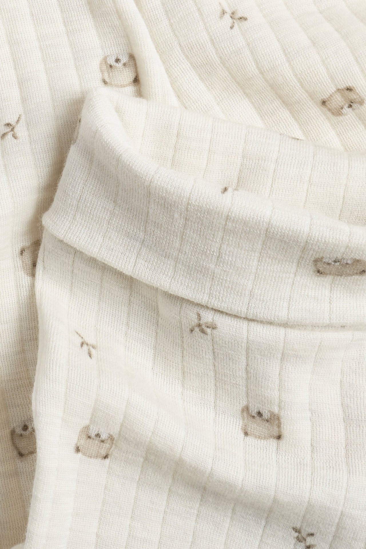 Nahaufnahme von beigemelange gerippten Woll-Leggings mit dezentem Tiermuster und umgeschlagenem Bündchen.