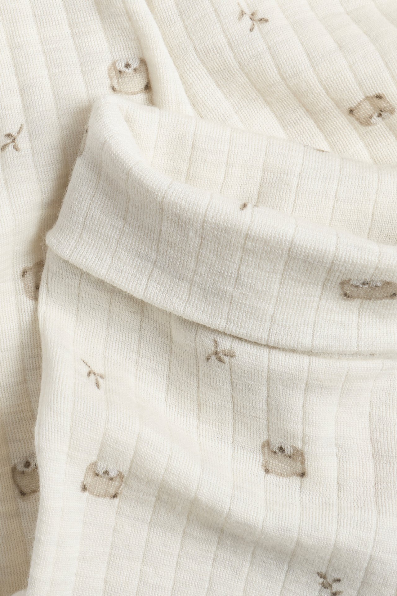 Nahaufnahme eines gefalteten hellcremefarbenen gerippten Babykleidungsstücks mit kleinem braunem Tiermuster.
