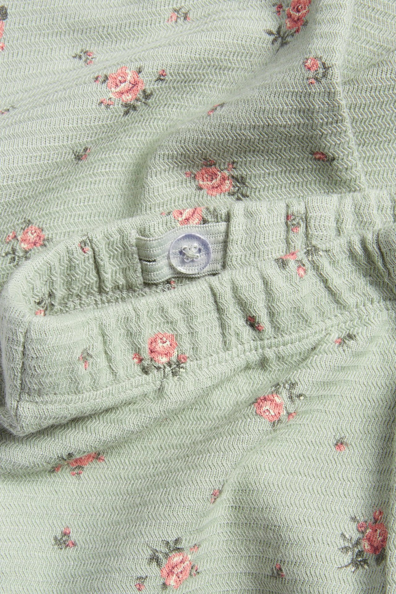 Nahaufnahme grüner strukturierter ausgestellter Leggings mit kleinem rosa Blumenmuster und verstellbarem Knopfverschluss.