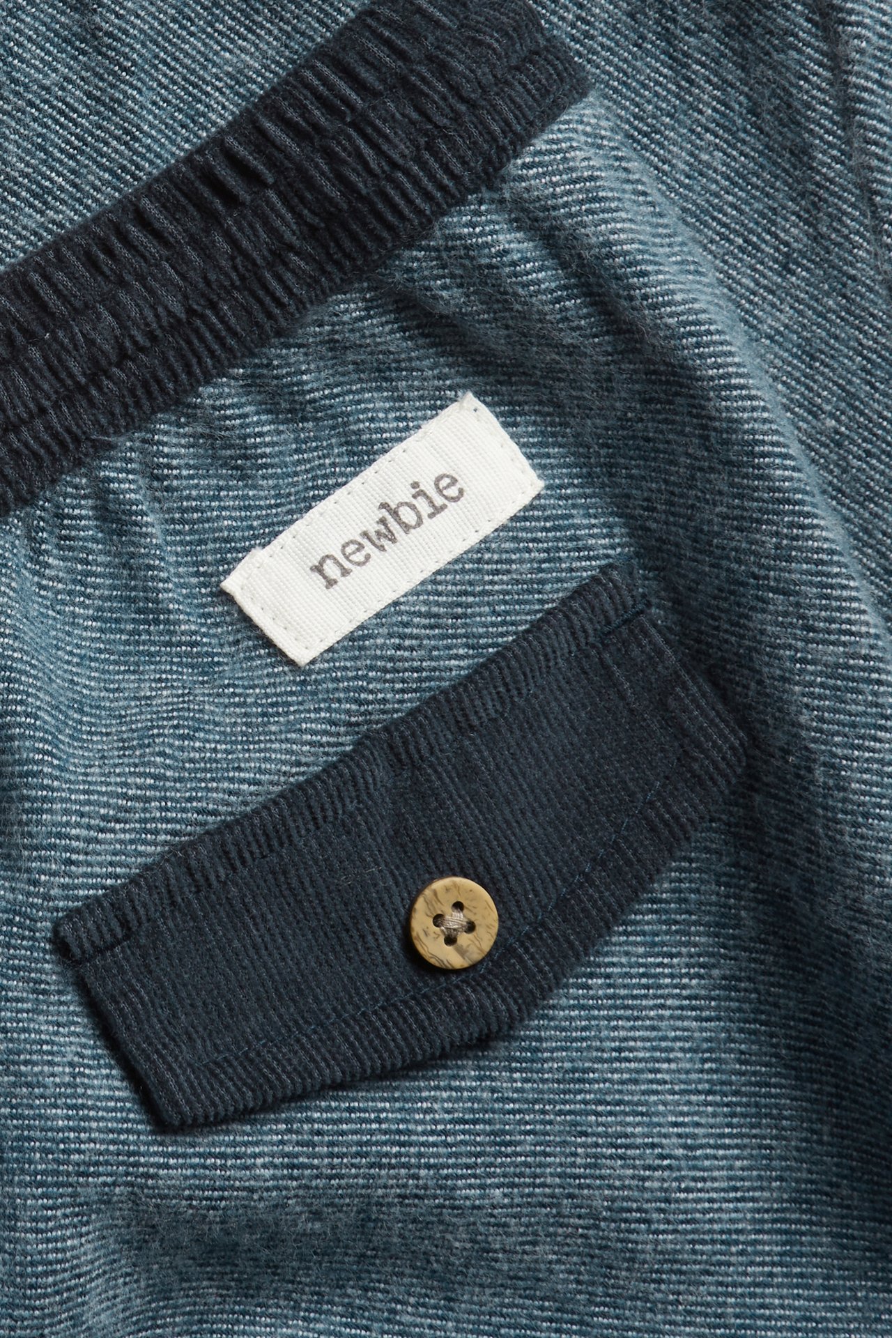 Close-up of dark blue woven twill trousers with a corduroy detail and wooden button.