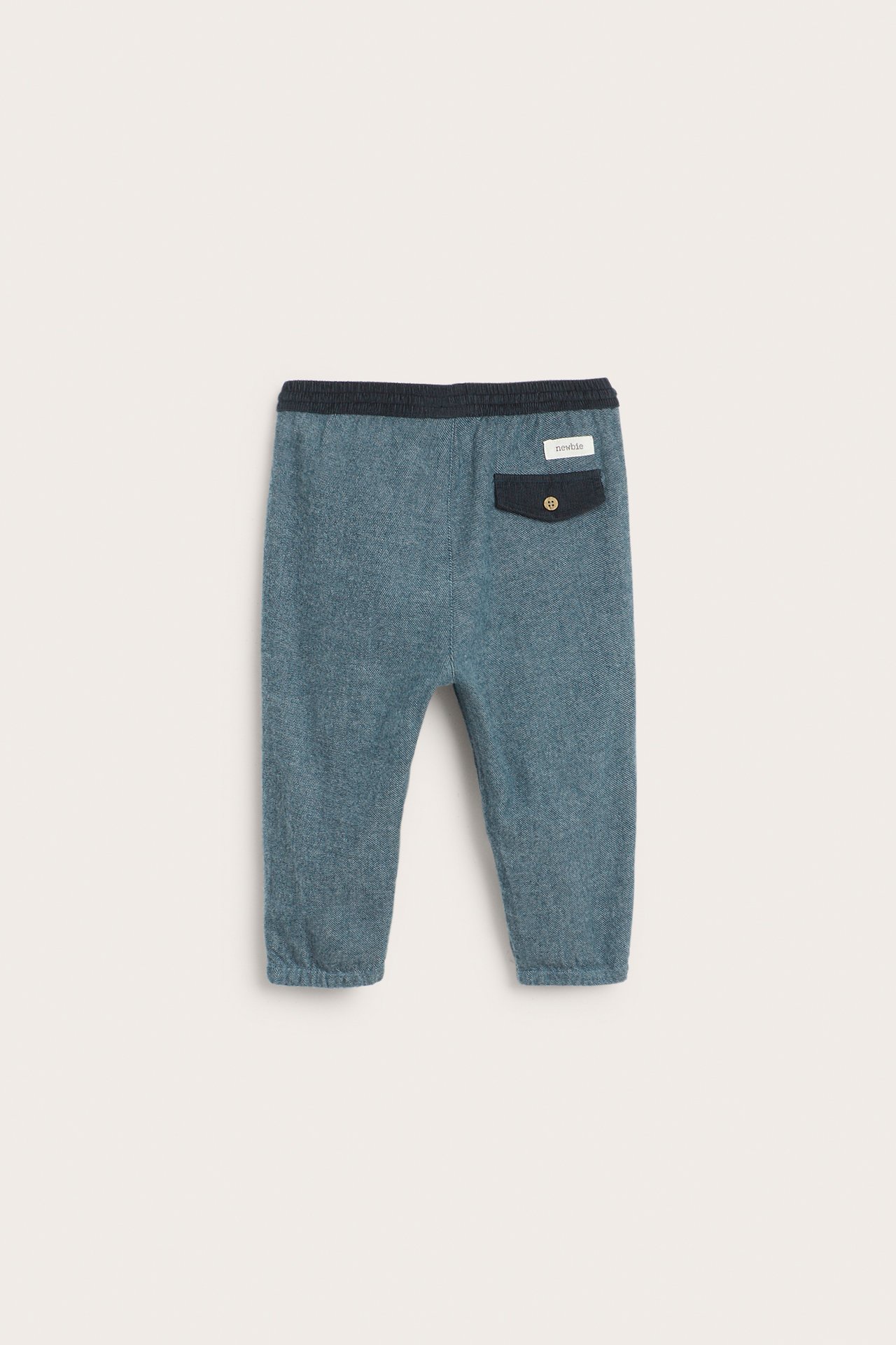 Back view of dark blue woven baby pants with a corduroy waistband and a buttoned back pocket.