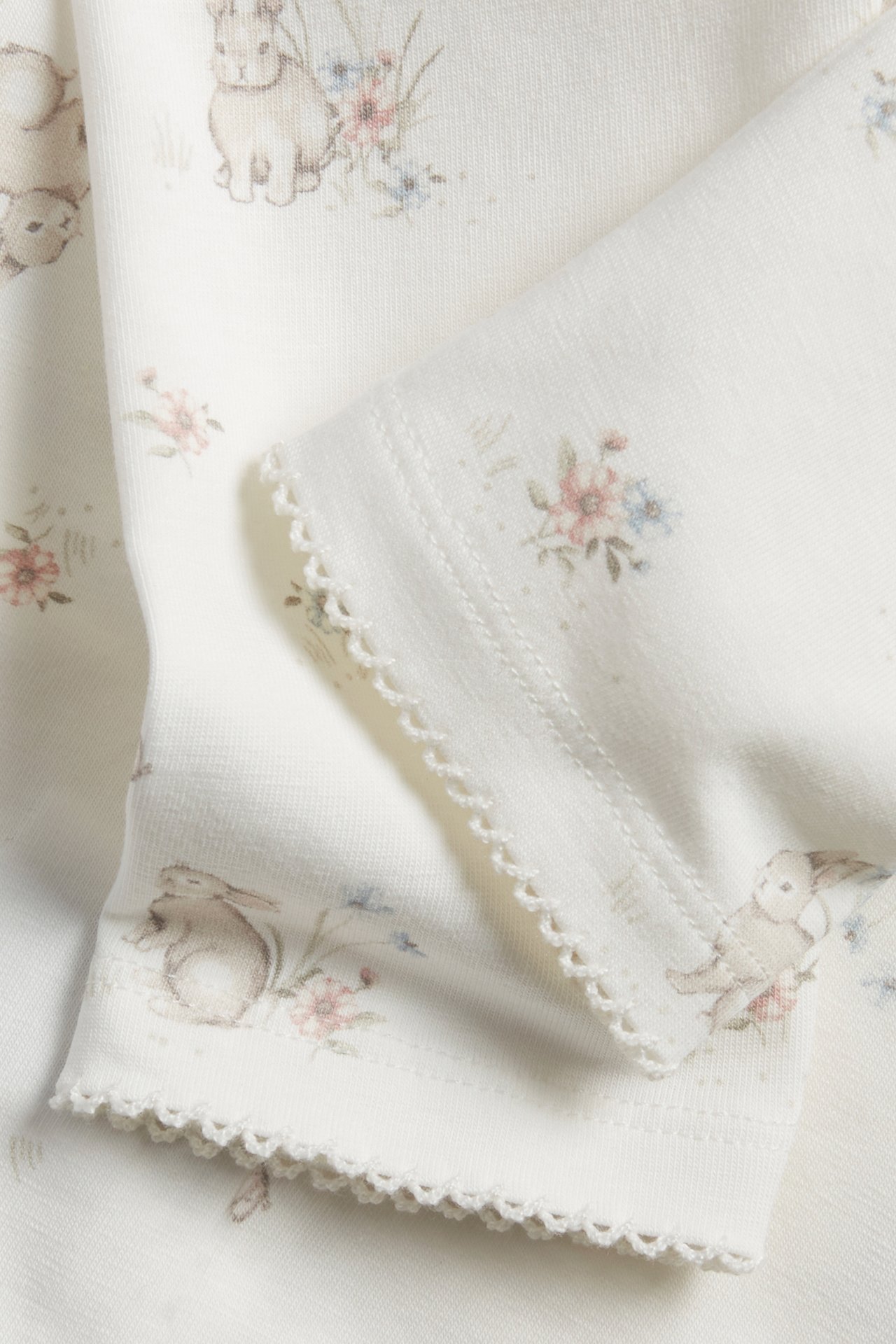 Close-up of off-white cotton blend leggings with a rabbit and floral pattern, featuring picot stitch cuffs.
