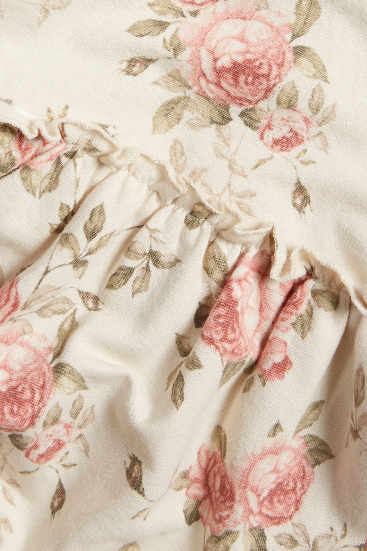 Close-up of light beige jersey dress fabric with pink rose floral pattern and ruffle detail.