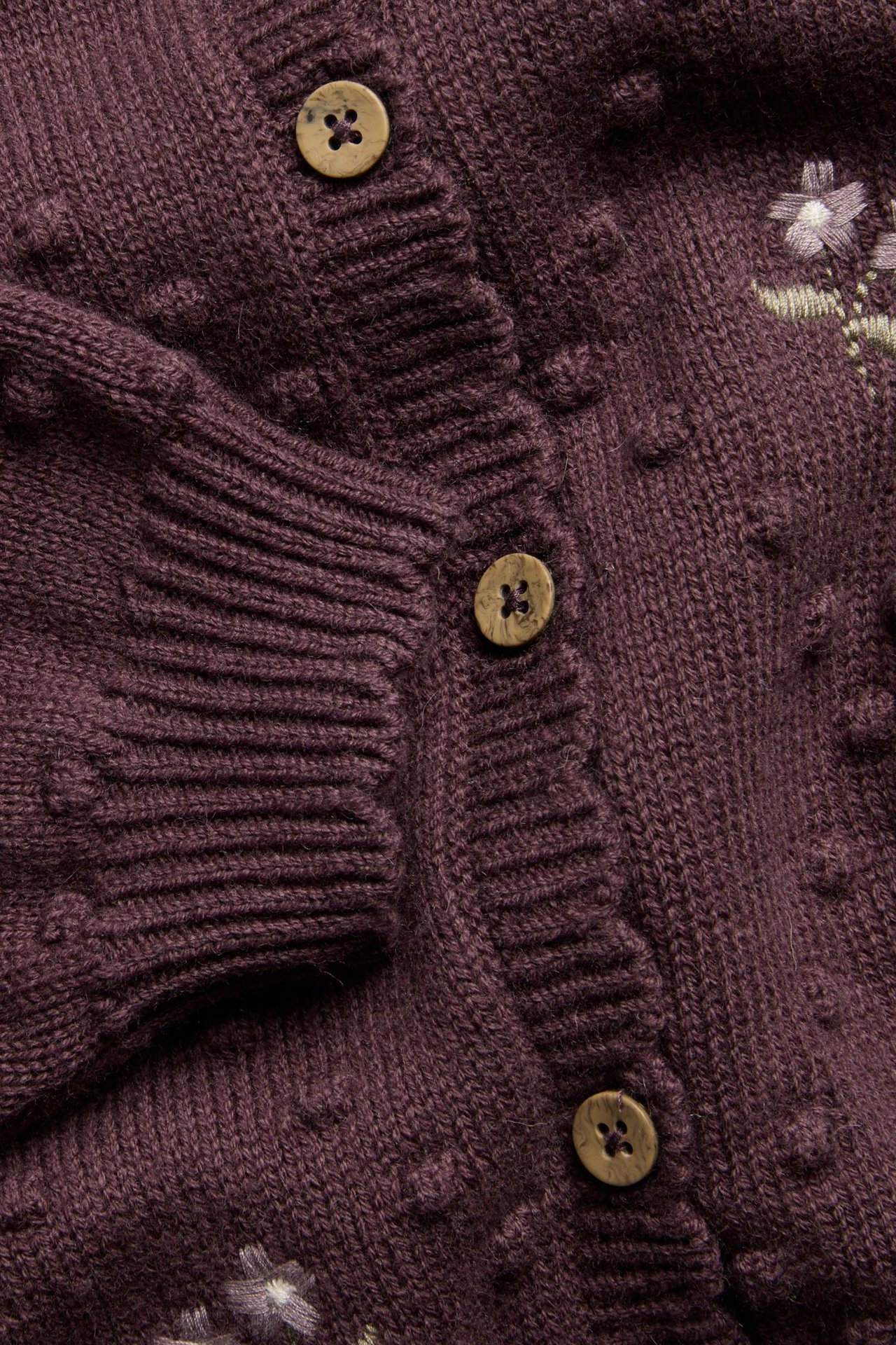 Nahaufnahme einer dunkelvioletten Wollmisch-Strickjacke mit Strickpunkten, gestickten Blumen und Holzknöpfen.