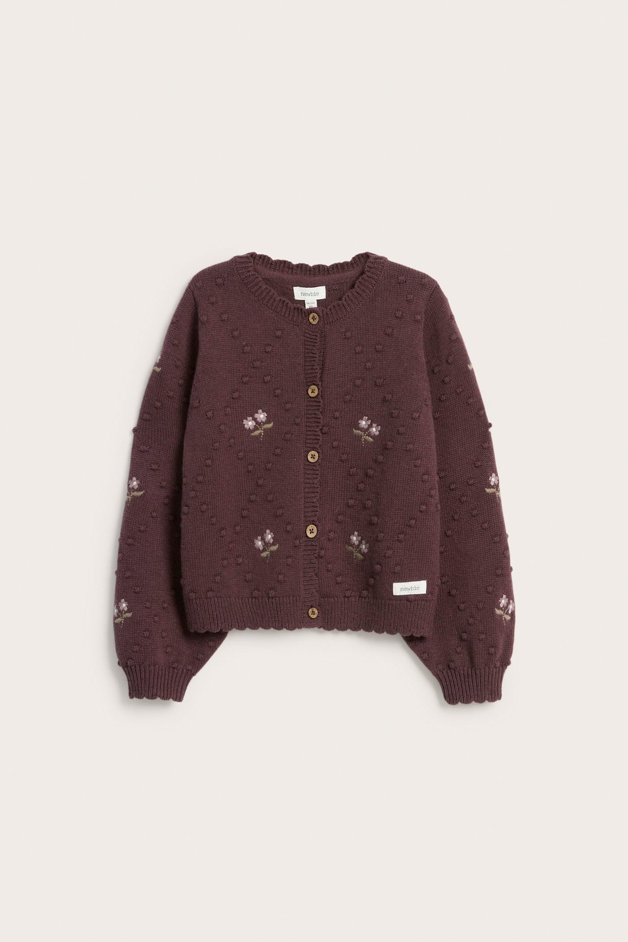 Vorderansicht einer pflaumenfarbenen Kinder-Wollmischstrickjacke mit Stricknoppen, gestickten Blumen und braunen Knöpfen.