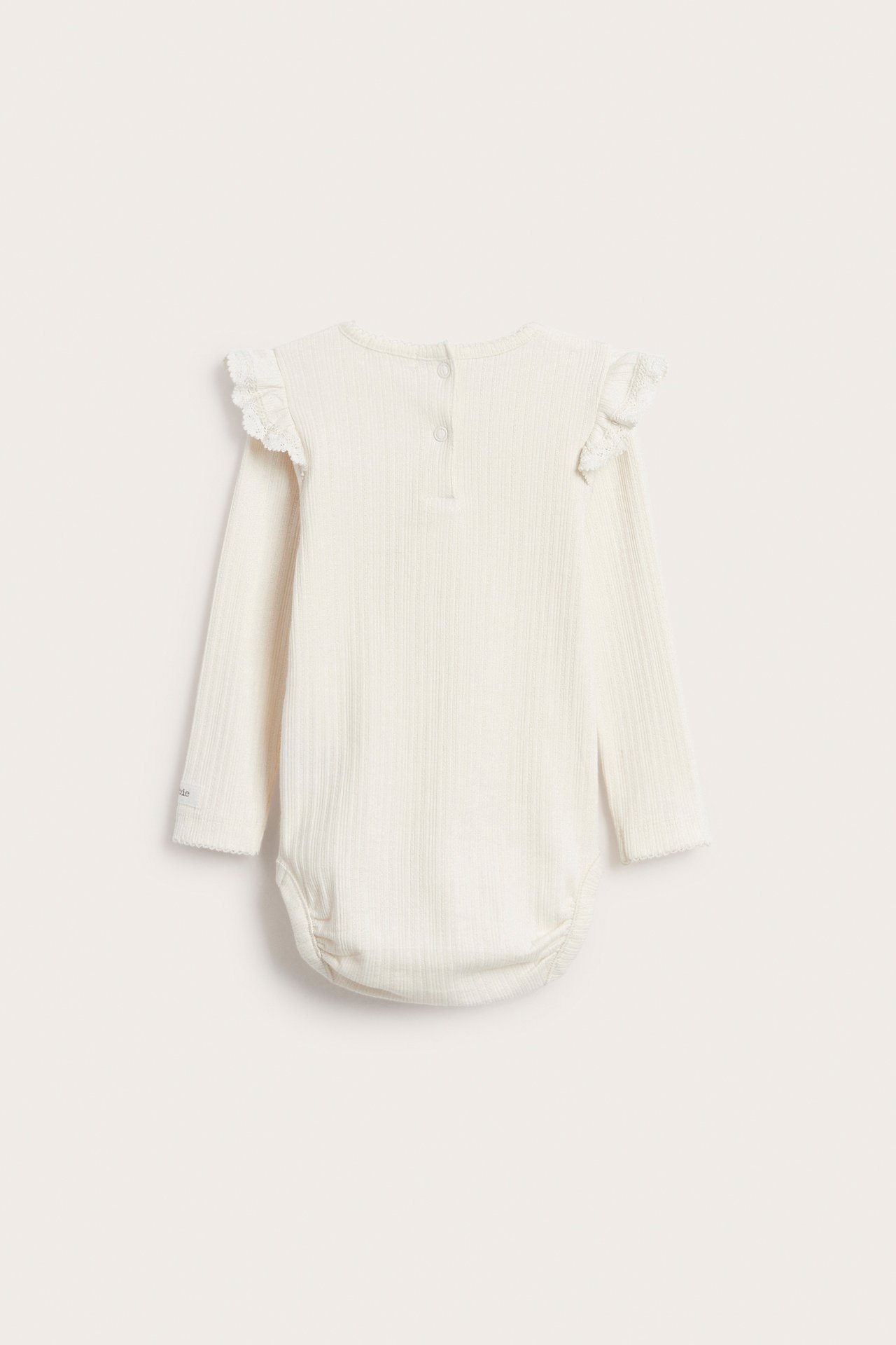 Rückenansicht eines gerippten, cremeweißen Baby-Langarmbodys mit Rüschen und Druckknöpfen.