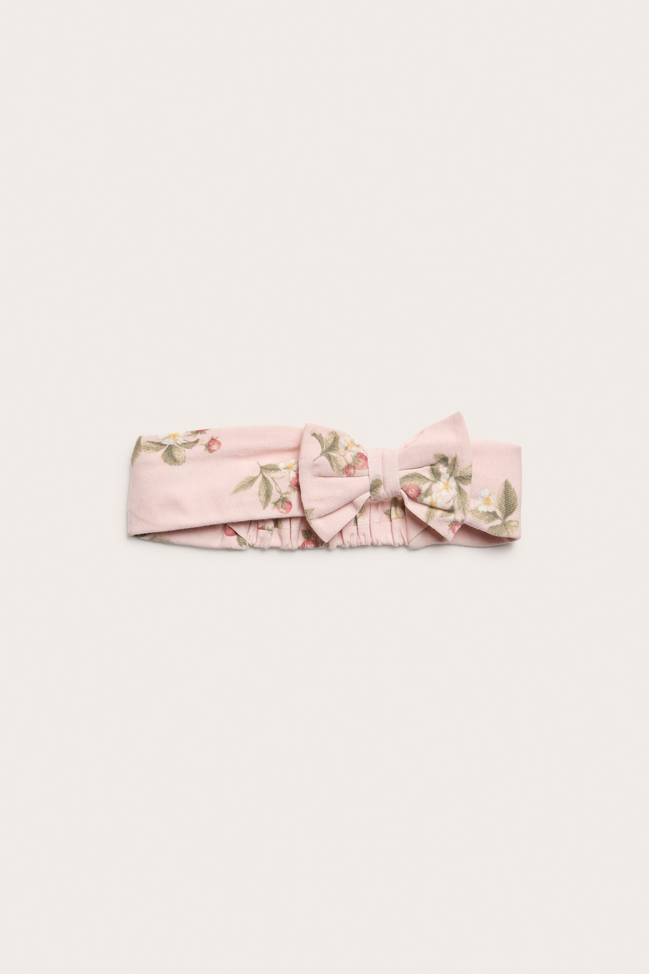 Front view of a light pink cotton jersey headband with a strawberry pattern and a bow.