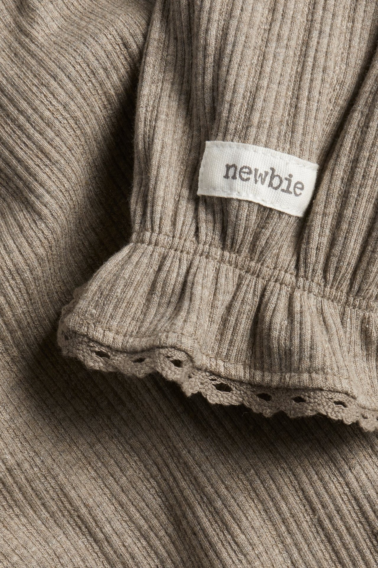 Close-up of a brown melange ribbed body with a ruffled, lace-edged cuff and a 'newbie' tag.
