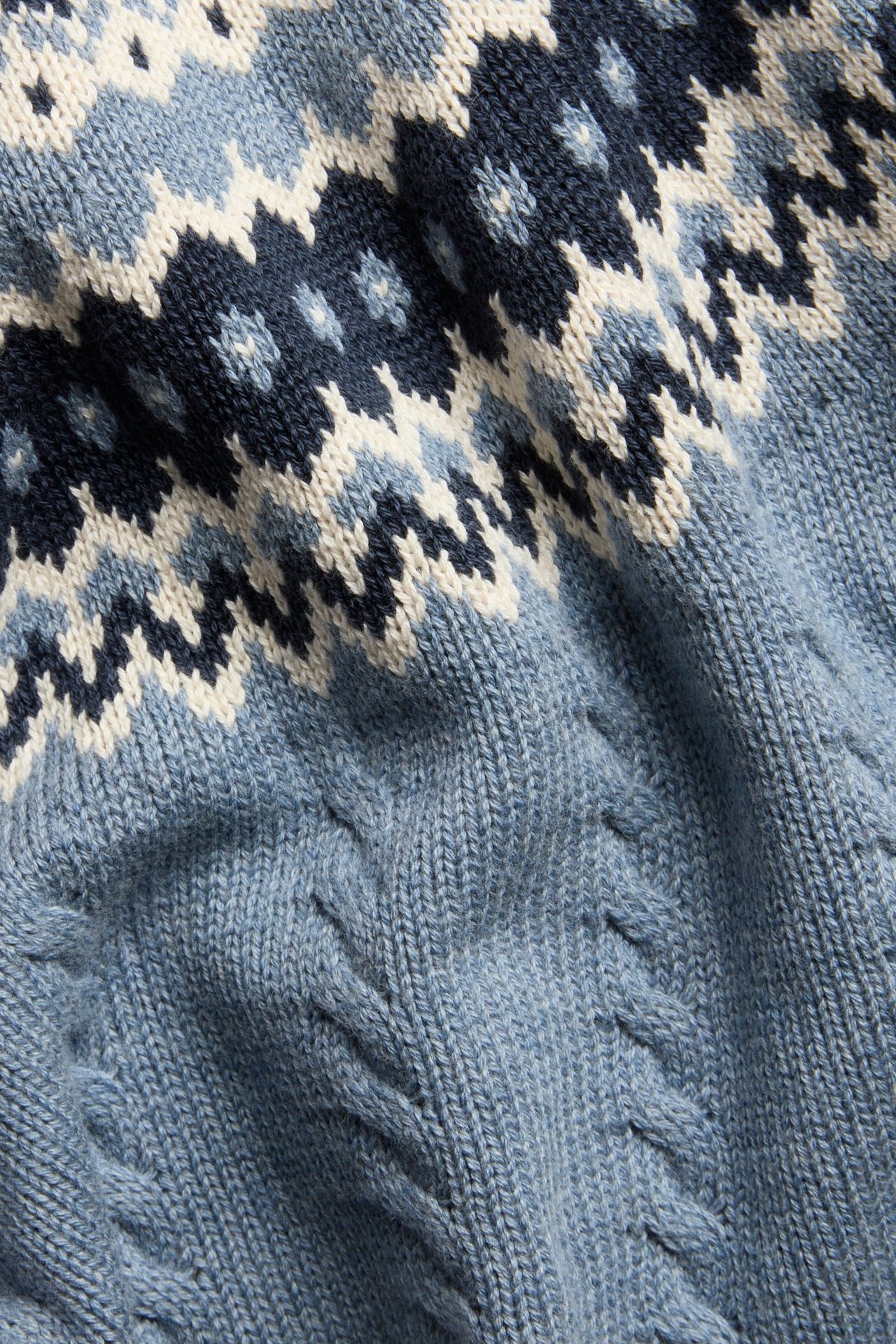 Nahaufnahme eines blauen gestrickten Baumwollpullovers mit Jacquardmuster und Zopfstrickdetails.
