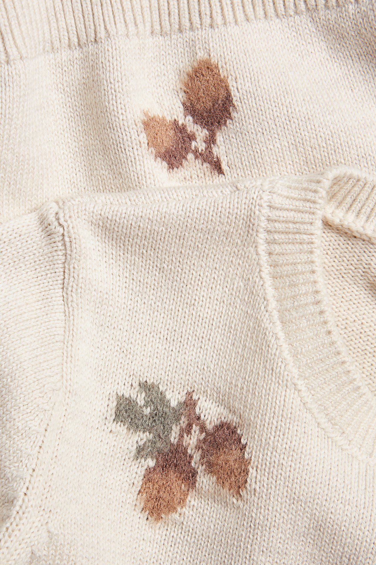 Nahaufnahme von zwei beigefarbenen Jacquard-Strickpullovern mit braunen und grünen Eichelmustern.