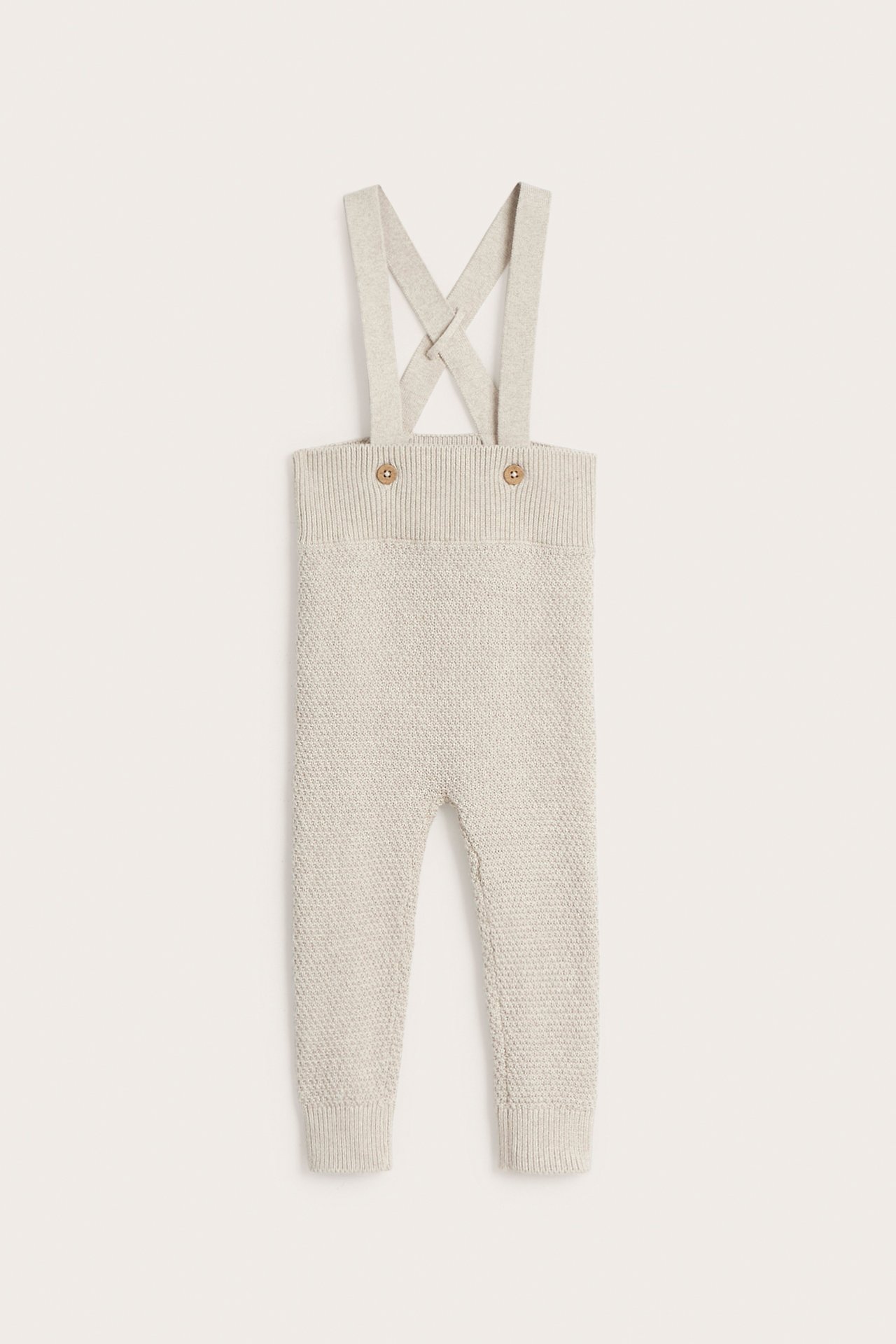 Vorderansicht von beigemelierter, strukturierter Baby-Latzhose aus Baumwolle mit verstellbaren Trägern und Holzknöpfen.