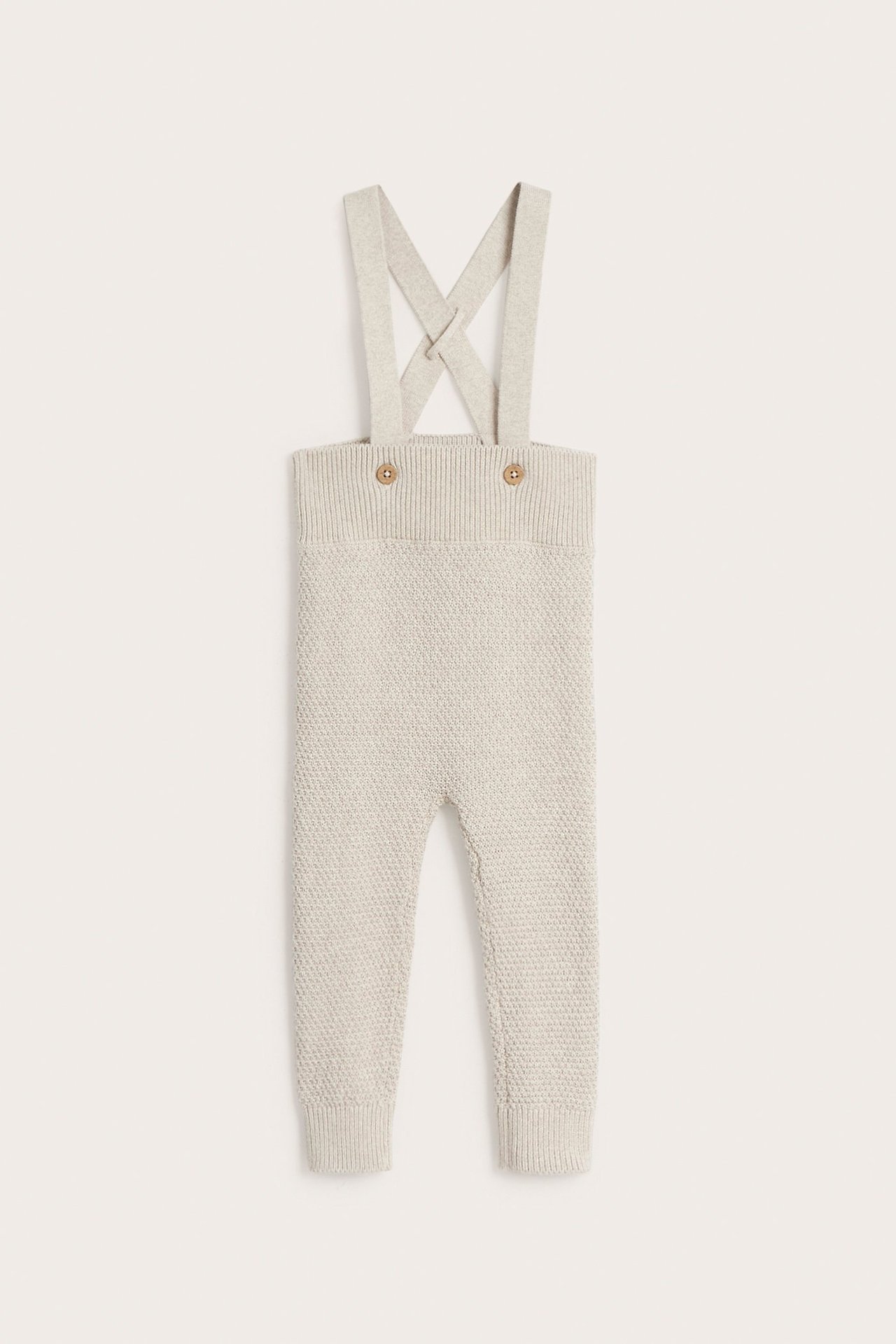 Vorderansicht von beigemelierter, strukturierter Baby-Latzhose aus Baumwolle mit verstellbaren Trägern und Holzknöpfen.