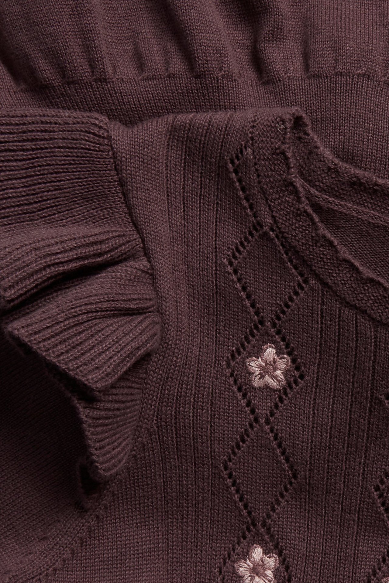 Close-up of a dark plum finely knitted cotton dress with ruffles, diamond openwork, and embroidered flowers.