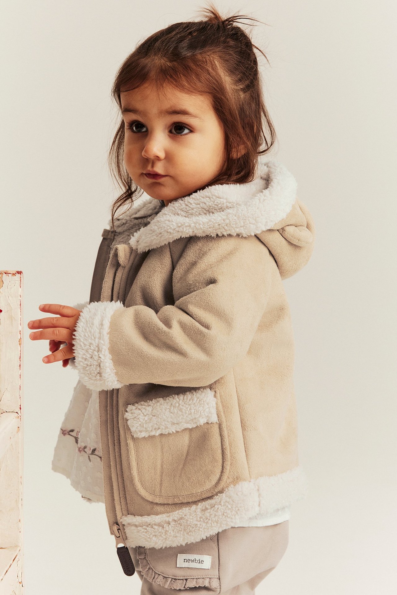 Seitenansicht eines Kindes in beiger Shearling-Jacke mit Teddyfutter, Kapuze und Bärenohren.