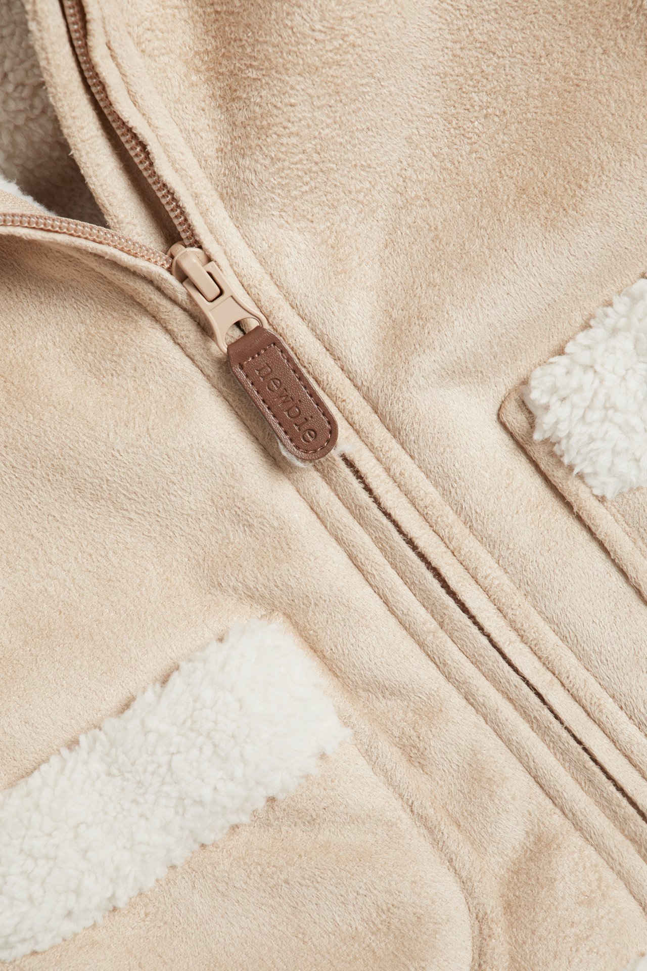 Close-up of a beige fake suede shearling jacket with white pile lining and a zipper.
