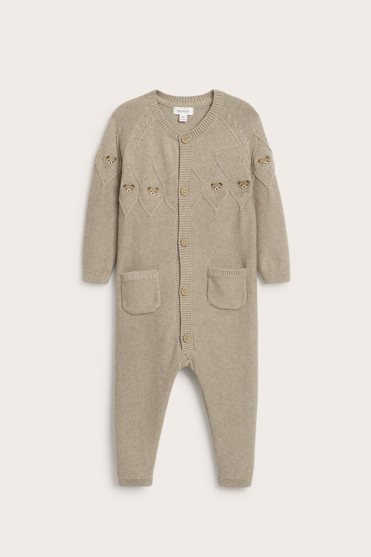 Vorderansicht eines beigen, strukturstrick Baby-Overalls aus Baumwolle mit Teddybär-Stickerei und Knöpfen vorne.